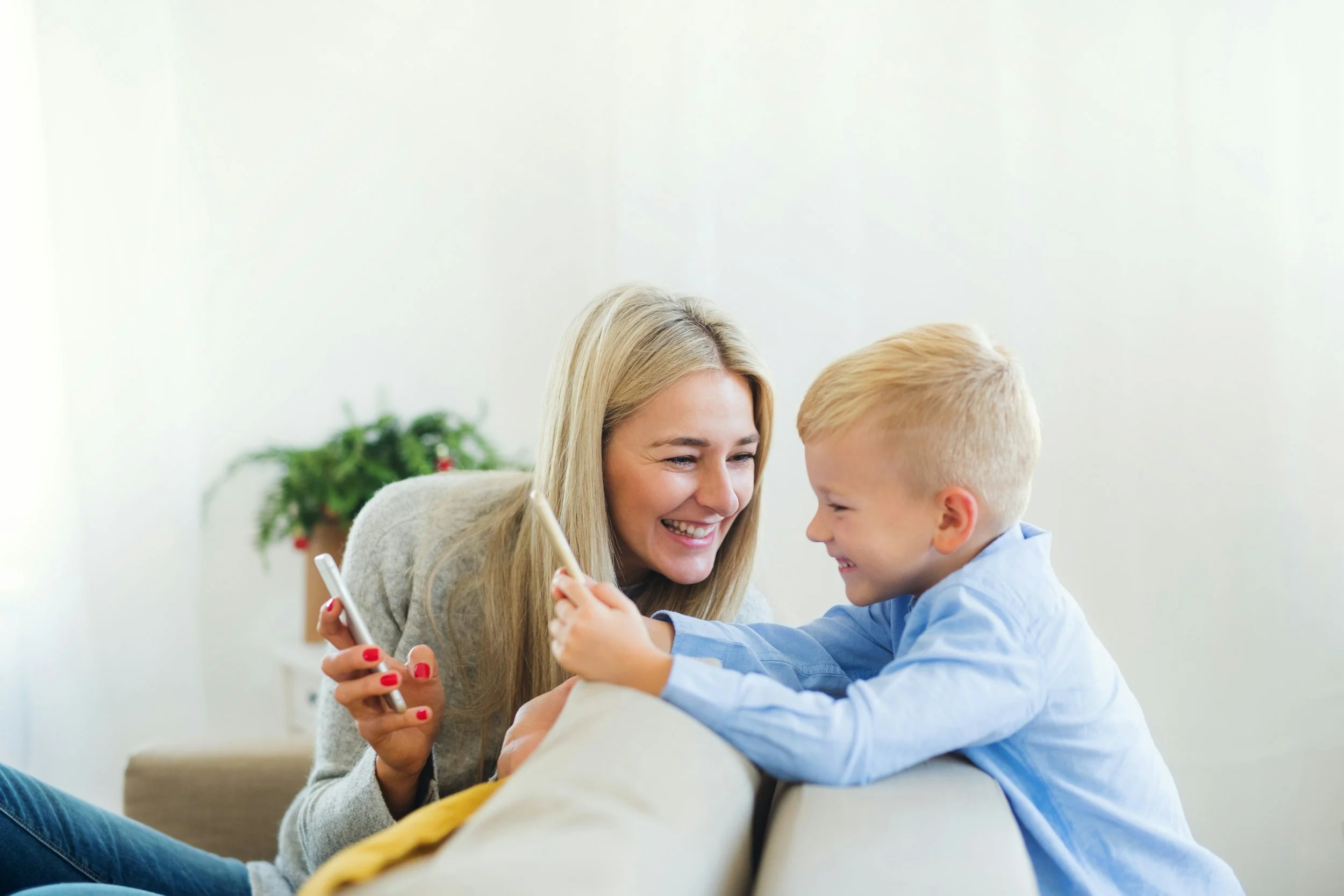 Mother and son smiling and using smartphones on a couch at home.