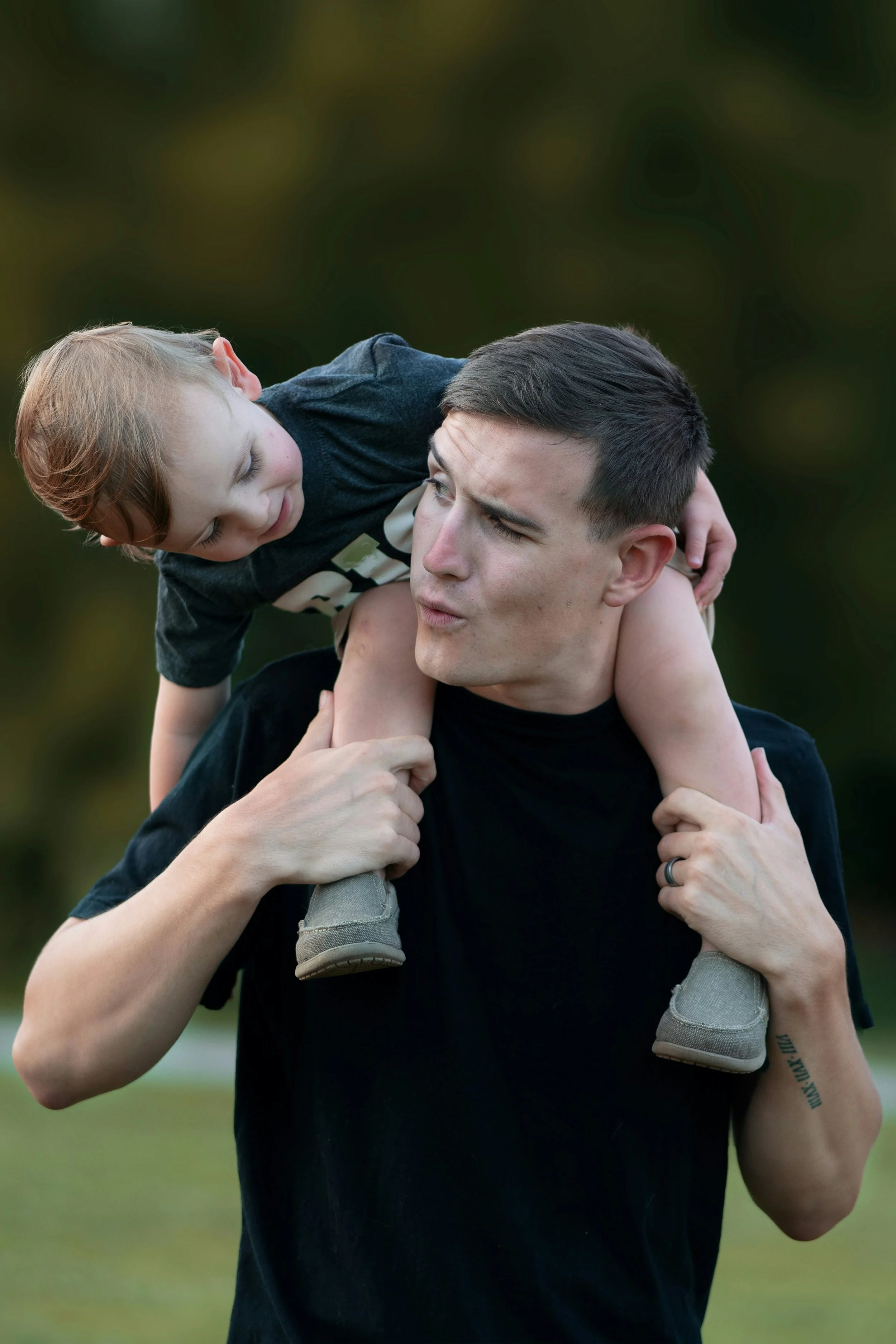 A man holding a child on his shoulders, both in casual clothing, outdoors.