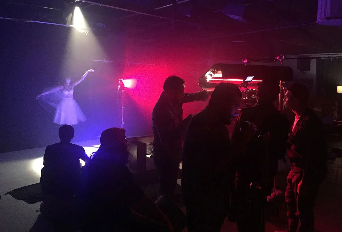 Dance studio with a ballerina performing under spotlight, and a Corgan Studio film crew filming her with colored lights and camera equipment. Directed by Jason Corgan Brown