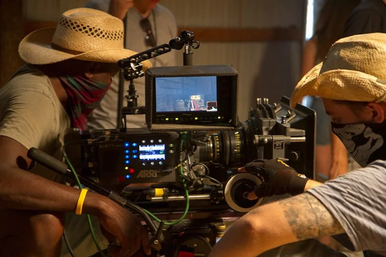 People wearing hats and masks working with a professional camera on a film set.
