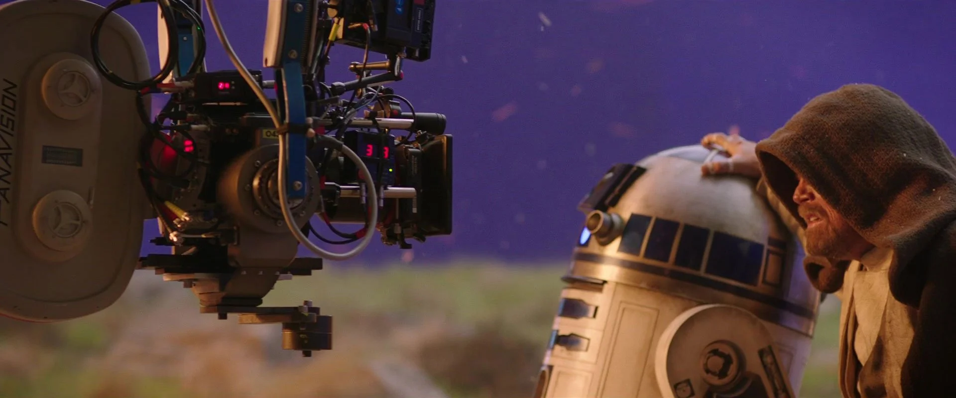 Mark Hamill as the Luke Skywalker character standing near R2-D2 with a camera and monitors mounted nearby, set against a night sky with stars. Jason Corgan Brown worked on the Star Wars film. 
