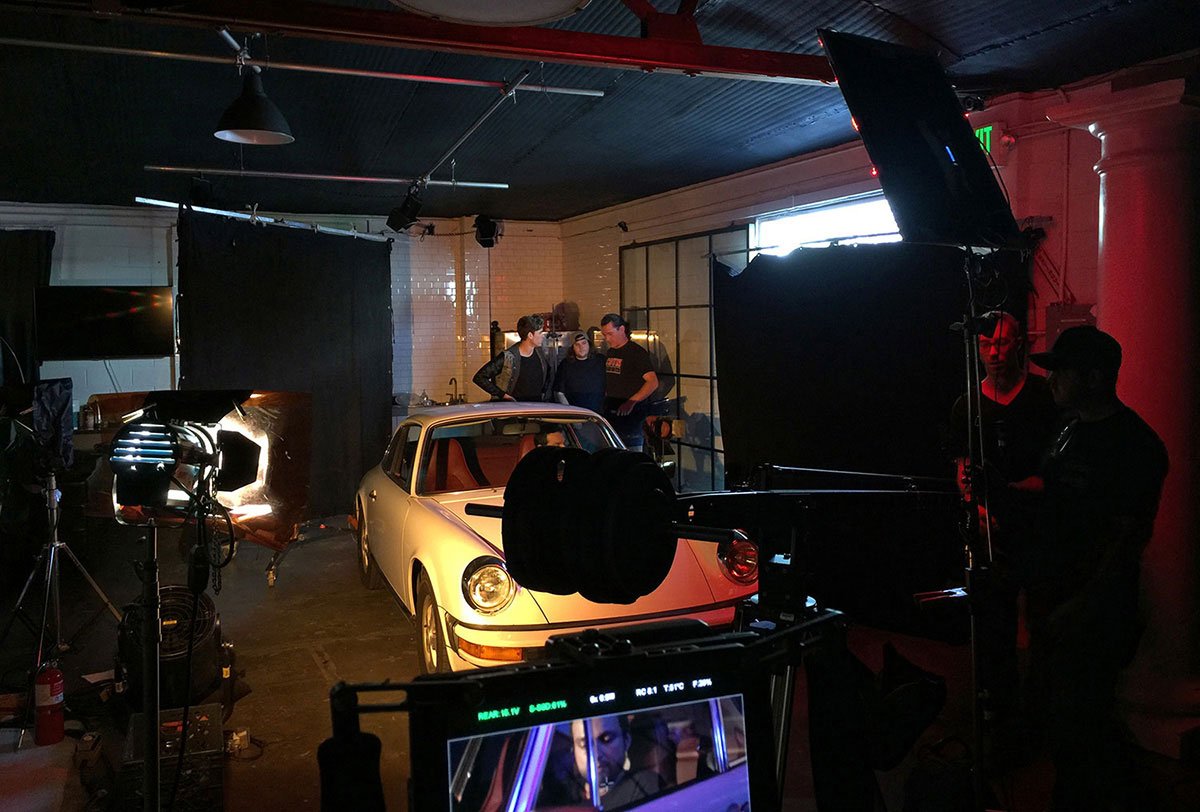 Behind the scenes of a film shoot by Corgan Studio with a vintage white Porsche car in a studio, crew members, and camera equipment.
