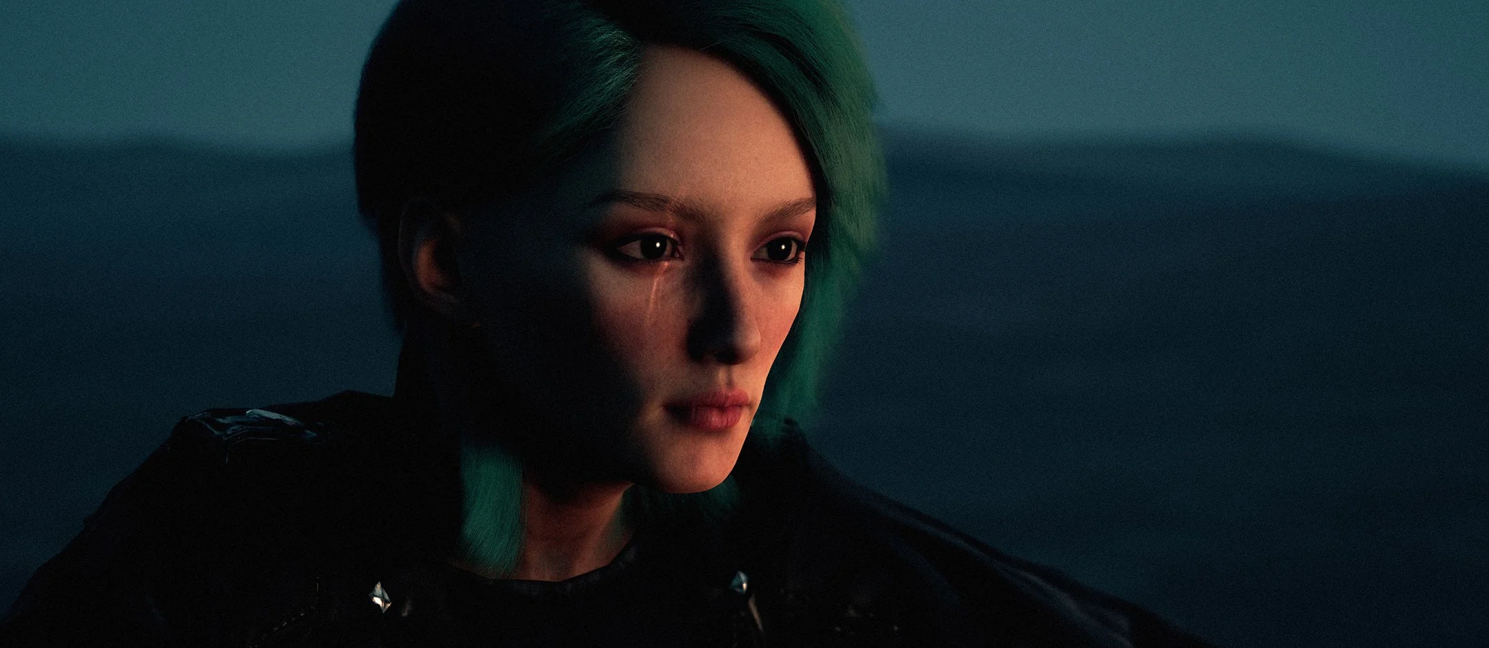 A young woman with short green hair looks thoughtful in a dimly lit setting, wearing a black leather jacket.