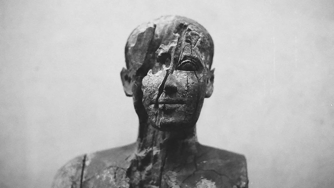 Wooden sculpture of a human face, partially damaged and cracked.