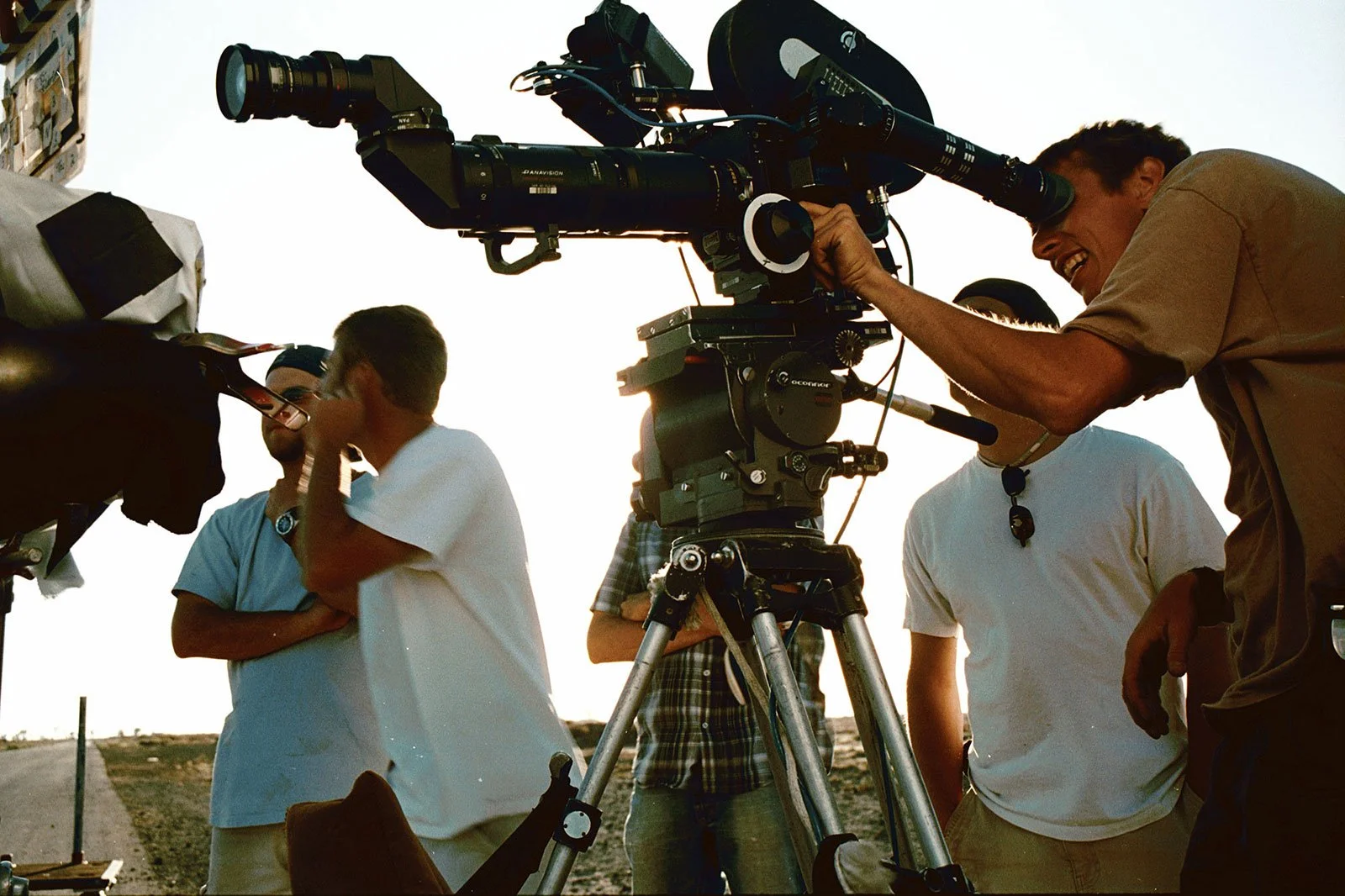 Filmmaking crew on set during sunset, operating a large professional camera on a tripod, with several crew members discussing and preparing for shoot. Produced by Jason Corgan Brown. 