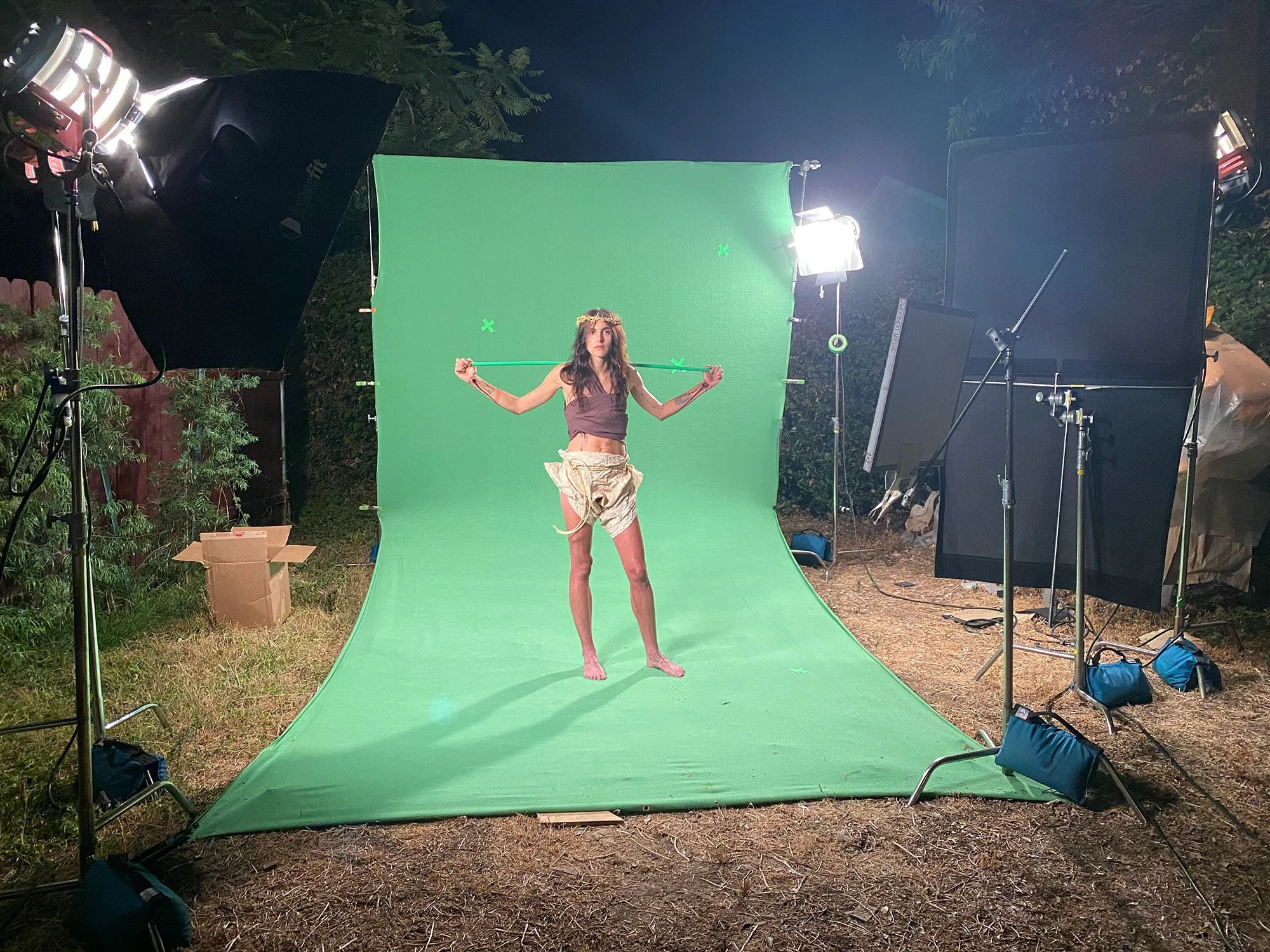 Langley Fox Heminway standing in front of a green screen, holding a stick behind her neck, on a Corgan Studio film set with lighting equipment. Directed by Jason Corgan Brown. 