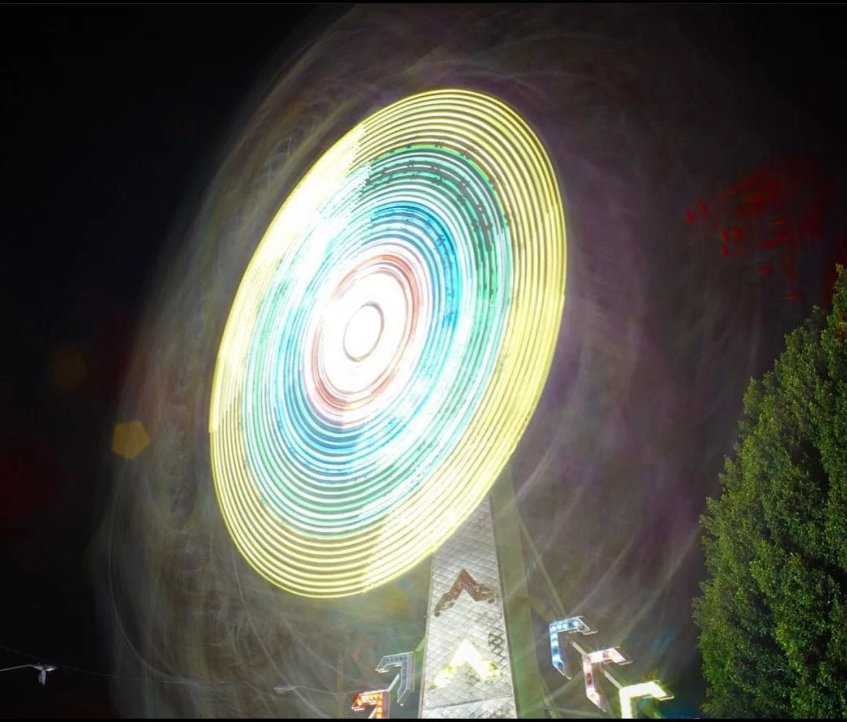 Nighttime shot of a brightly illuminated Ferris wheel with multicolored lights in motion.