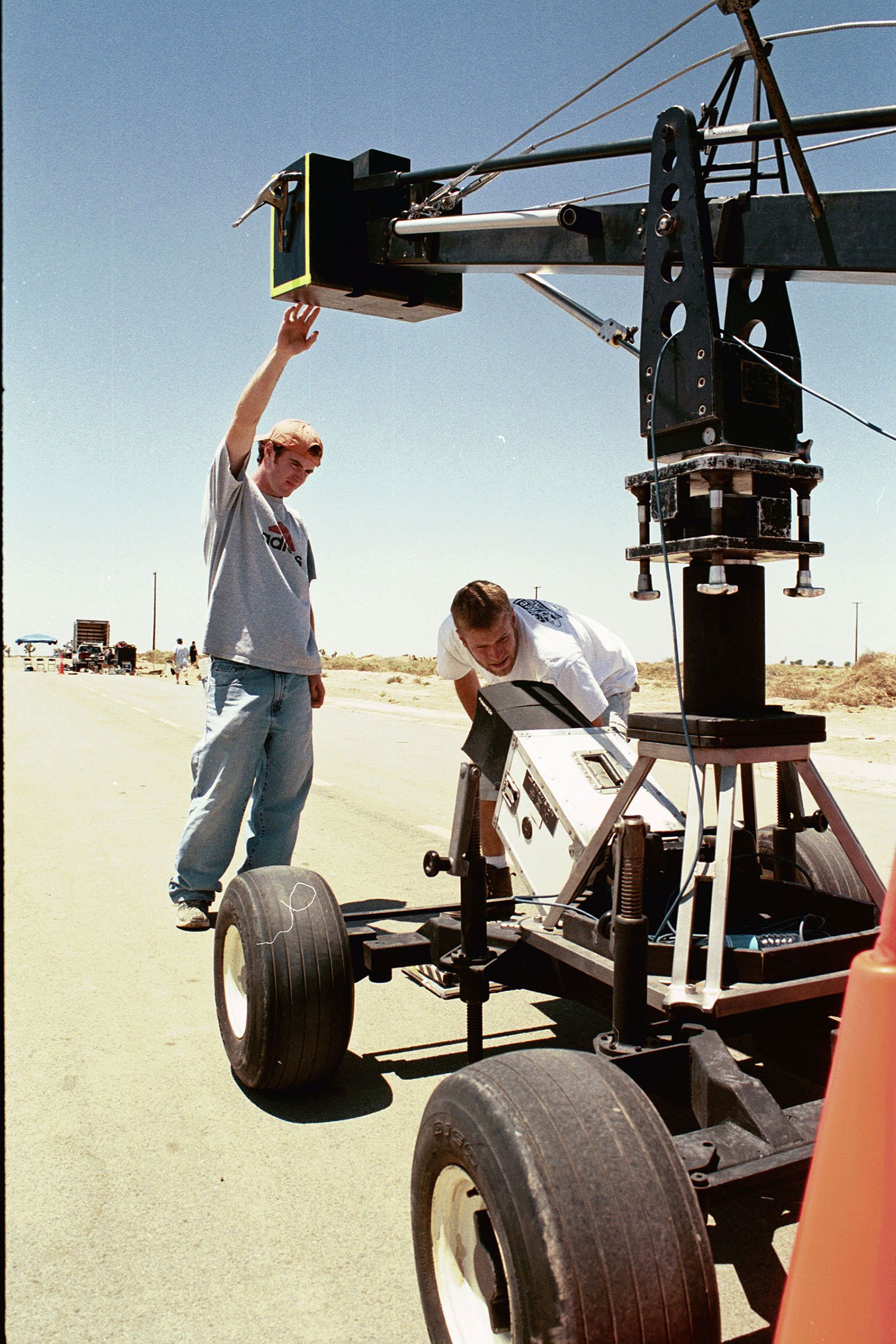 Film crew working on camera mounted on a small vehicle in a desert setting, with a clear blue sky overhead.
