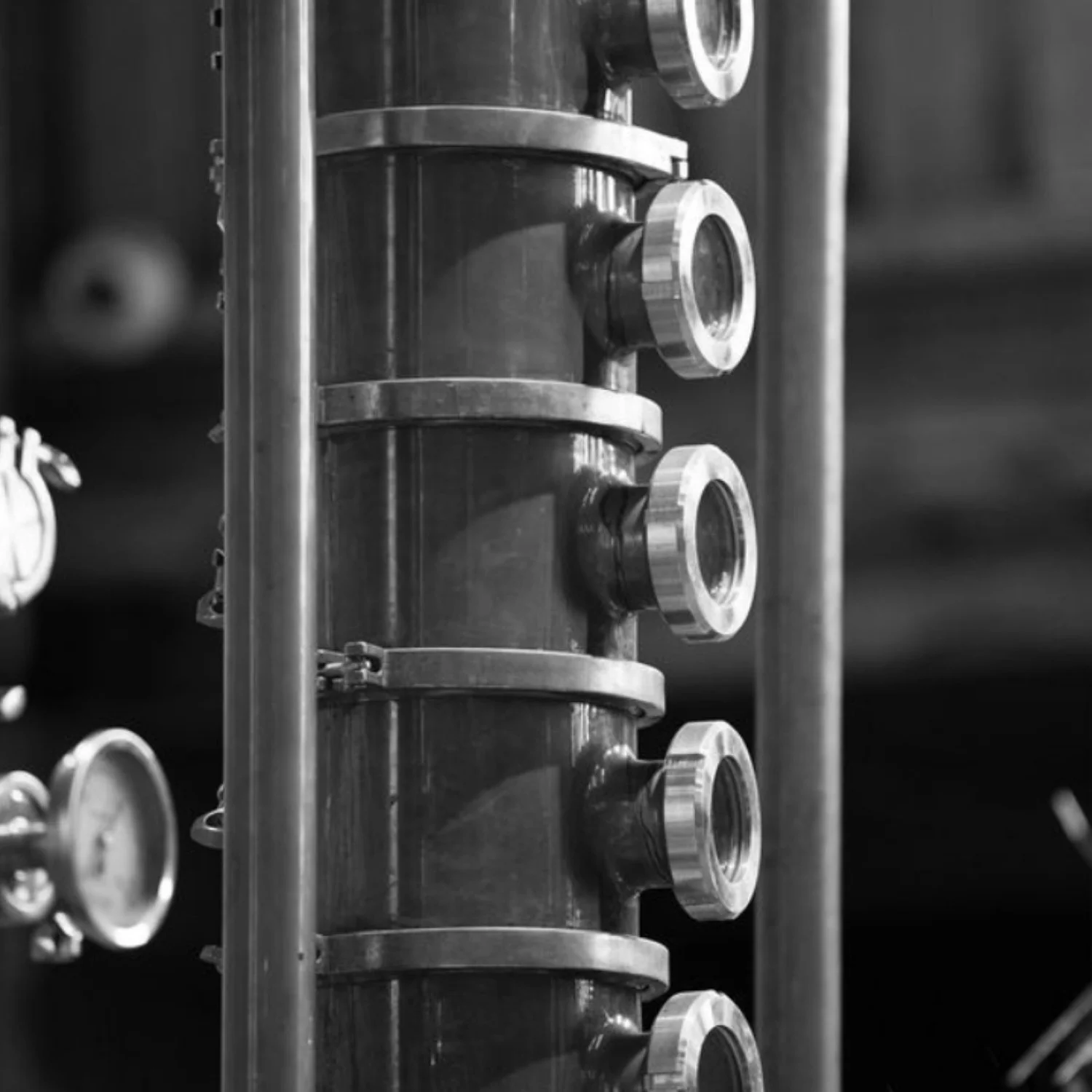 Close-up of industrial machinery with cylindrical components and adjustment knobs, in black and white.
