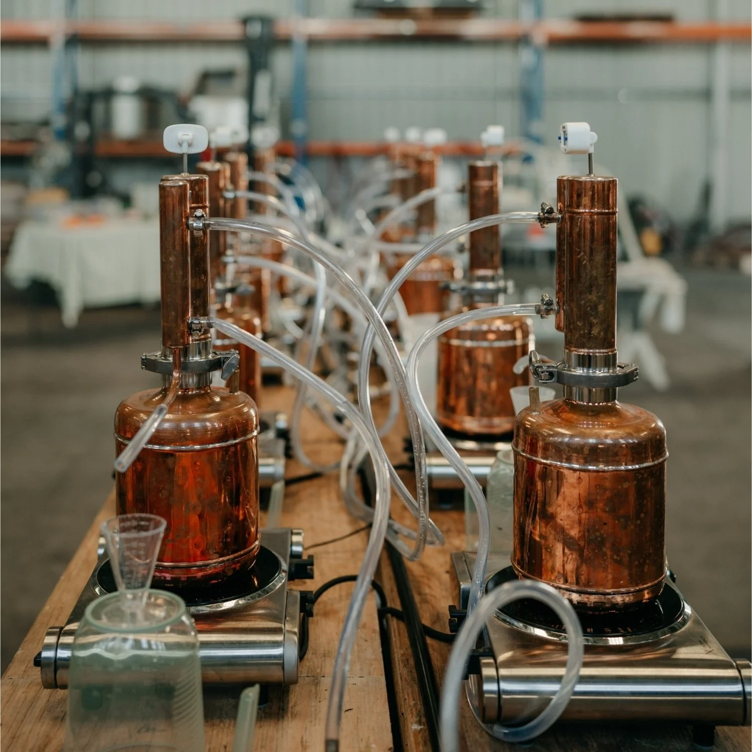 Copper distillation apparatus on a wooden table in a warehouse or workshop.