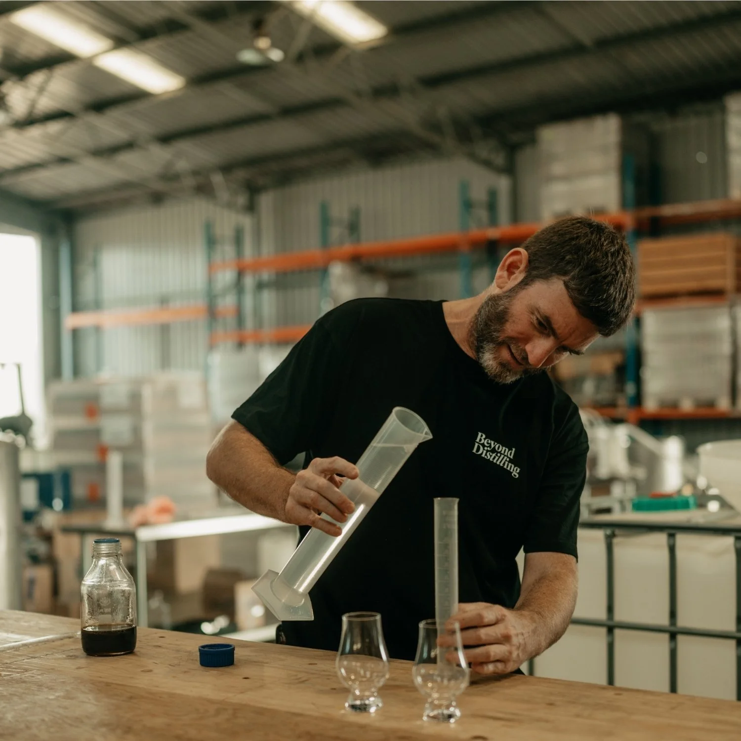 Man with a beard mixing ingredients in a distillery workshop.