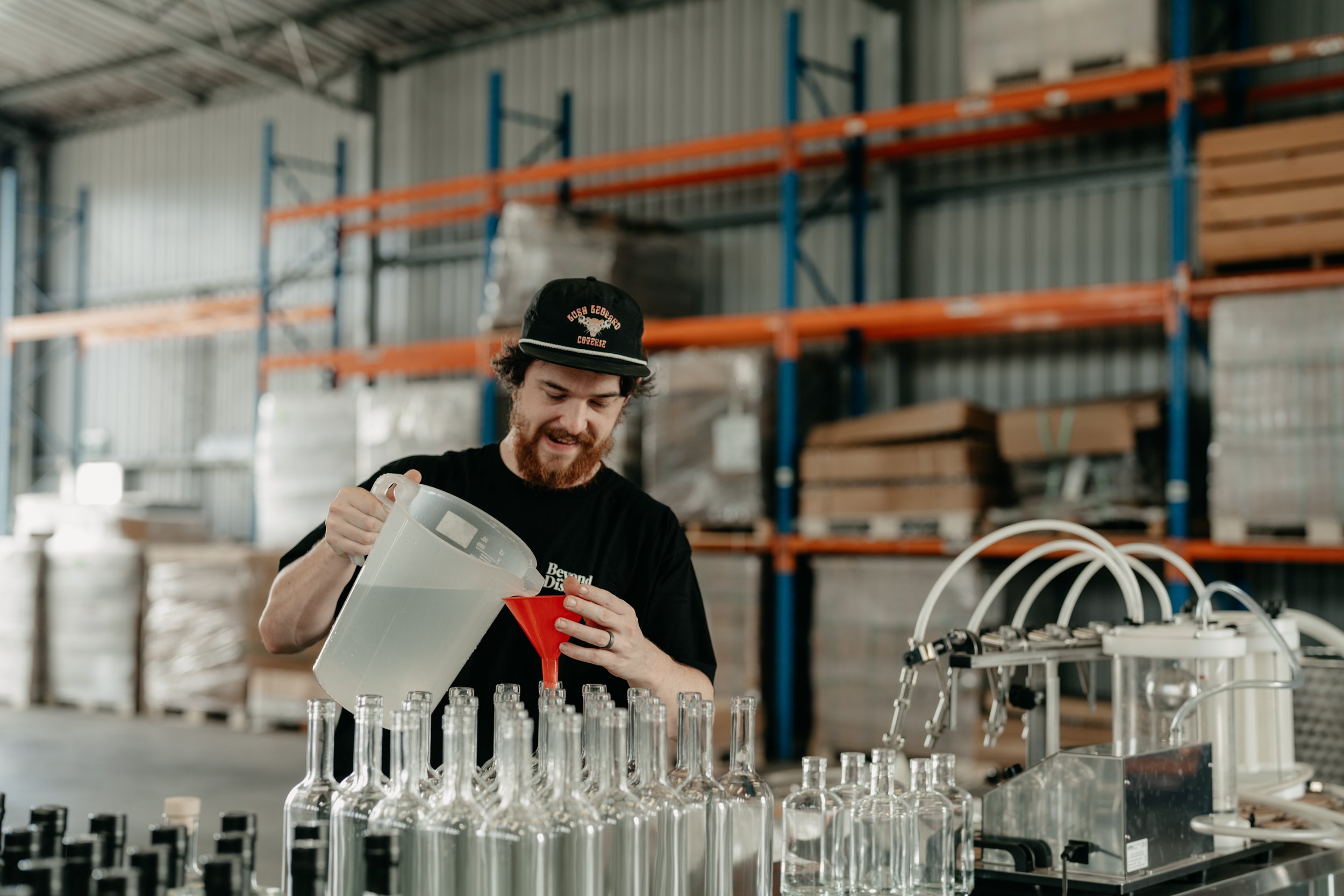 Man in a warehouse pouring liquid into bottles using a funnel