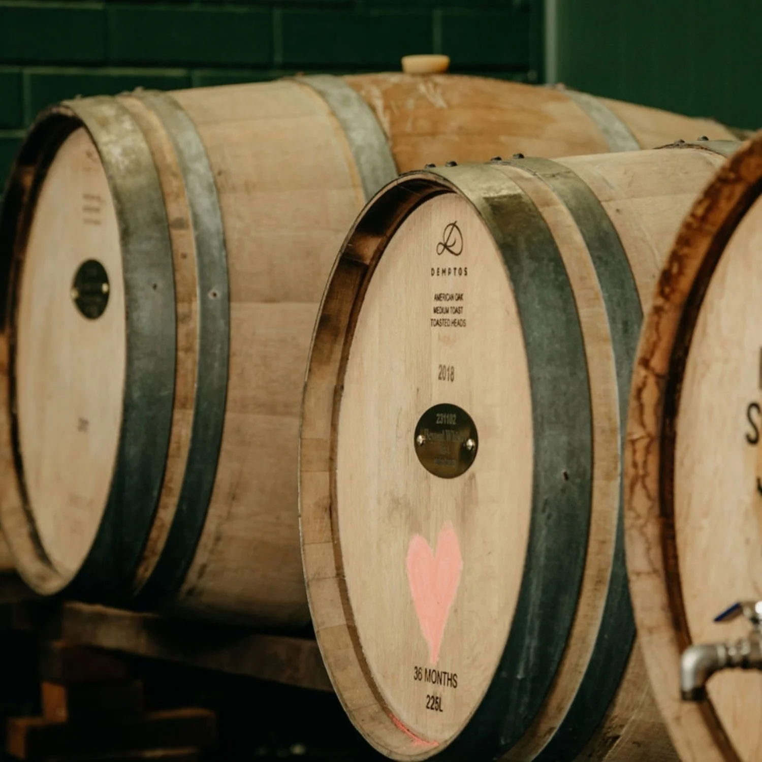 Wooden wine barrels labeled with brand and vintage, one with a pink heart graphic.