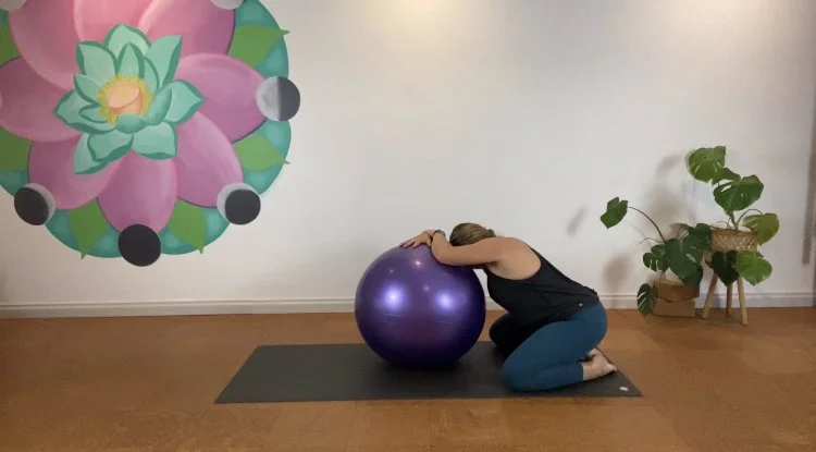 A pregnant woman practicing yoga or meditation under a beautiful moon mandala art work in Bloom Yoga, a boutique yoga studio in Perth's north.