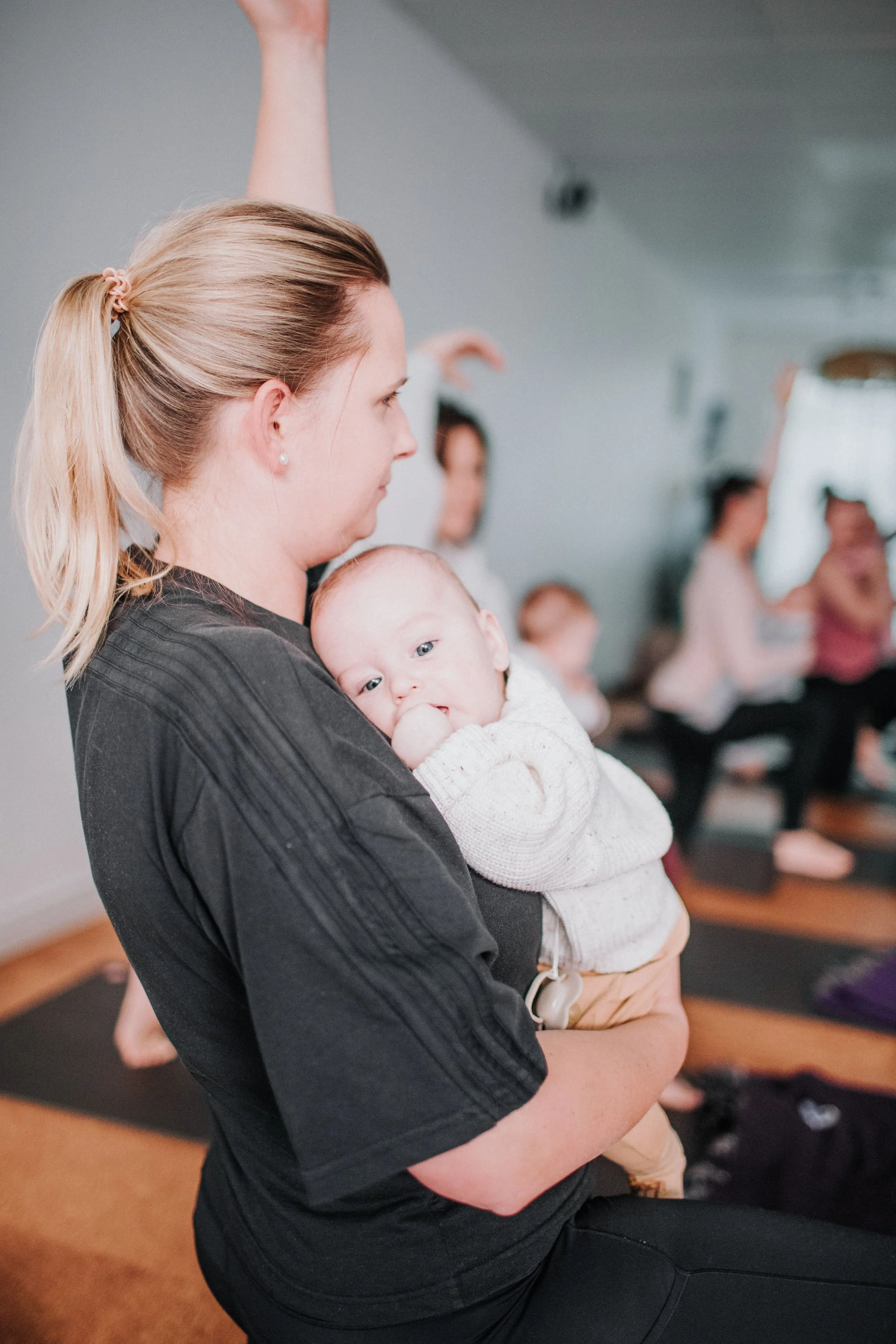 A new mum holding a baby during a postnatal yoga class with other new mothers at Perth Yoga Studio, Bloom Yoga.