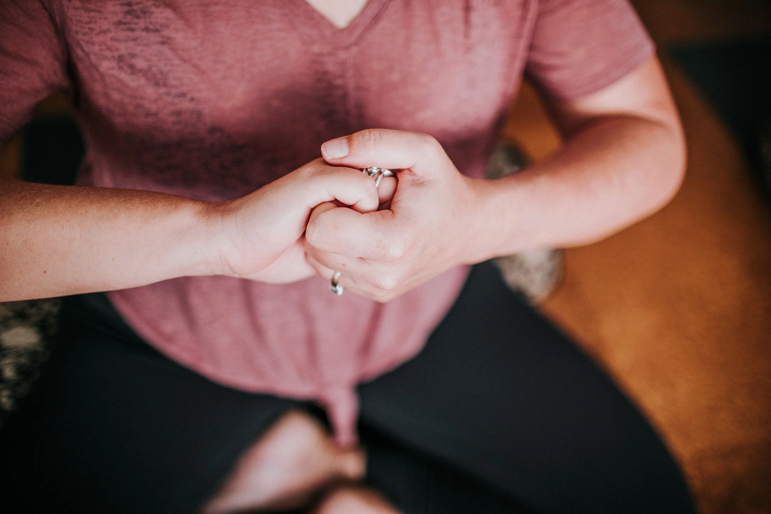 woman seated in a crossed legged yoga pose with fingers linked in a mudra at kingsley yoga studio