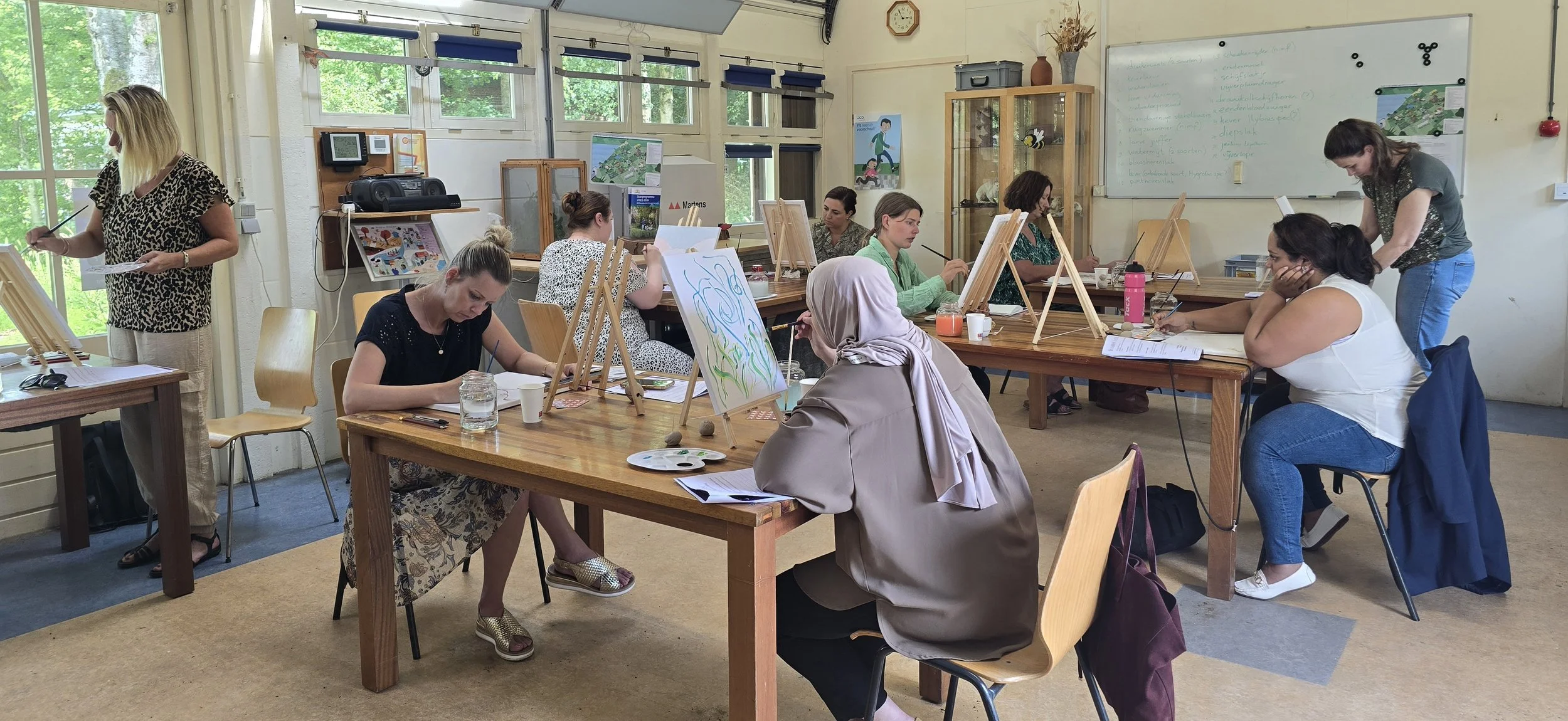 Mensen die in een schilderklas bezig zijn met hun kunstwerken, terwijl een instructeur hen begeleidt.