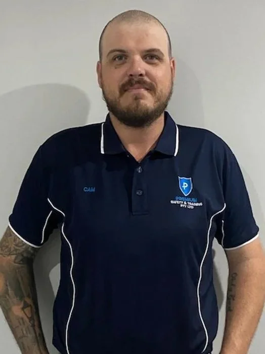 Man in navy blue uniform with safety training logo, standing against a plain light gray wall.