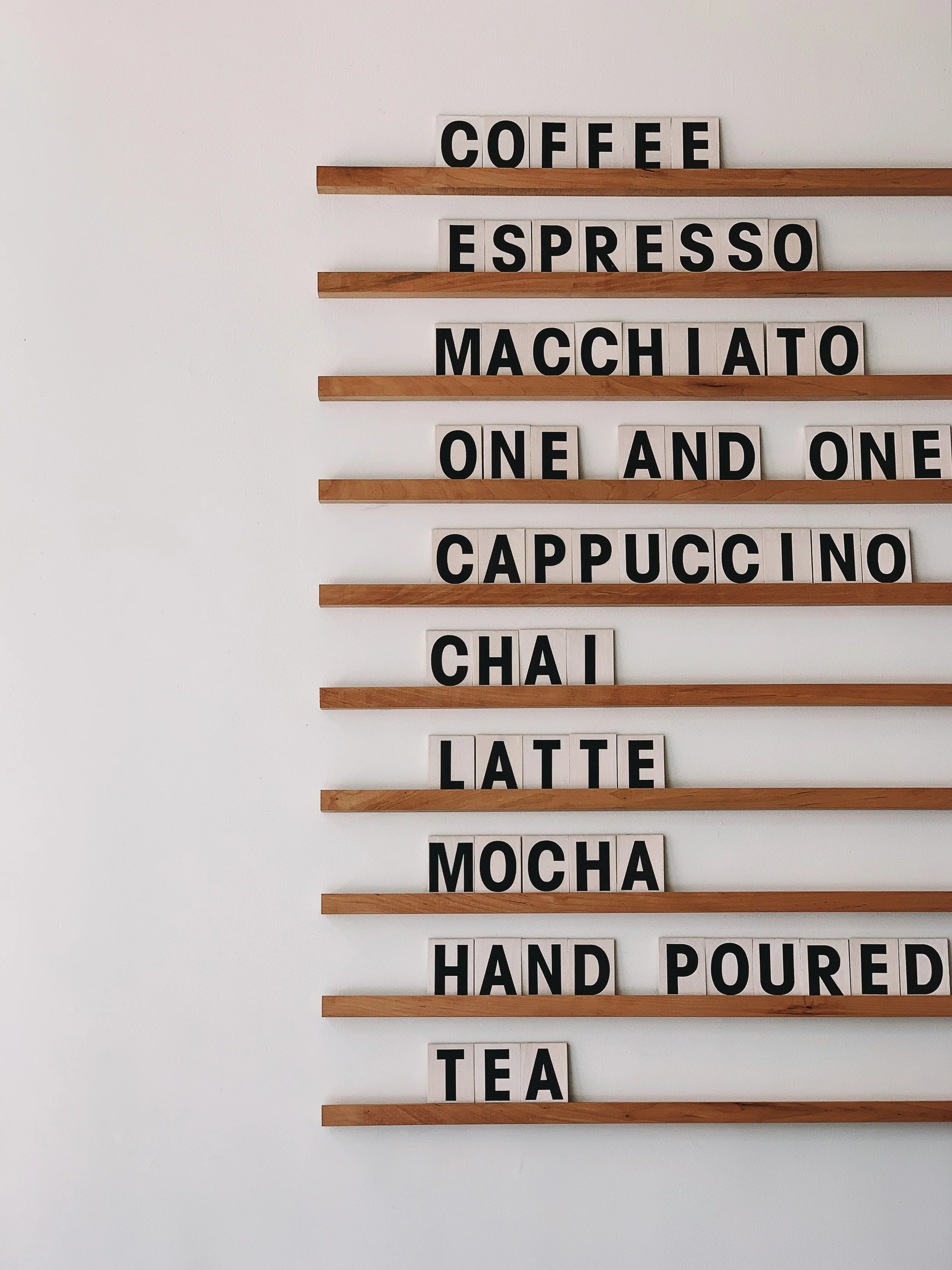 Coffee menu board with wooden shelves displaying items like espresso, macchiato, cappuccino, chai, latte, mocha, and tea.