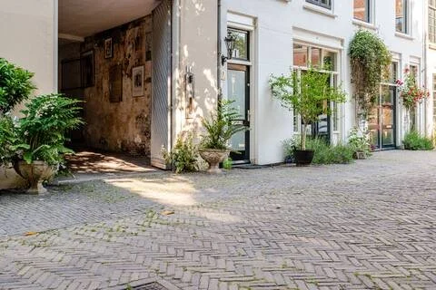 Een binnenplaats met bakstenen vloer en planten in potten voor de witte gevel van een gebouw.