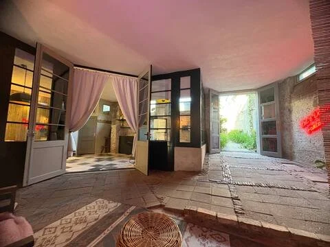Binnenruimte van een woning met open deuren naar een tuin, met decoratief tapijt, een rotan poef en een afdrijvingsvloer.