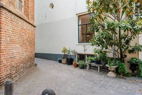 Een kleine binnenplaats met een brick muur, een wit gebouw en verschillende planten in potten.