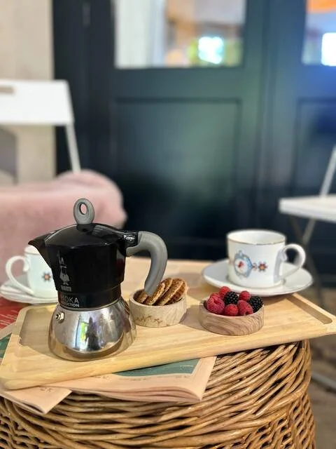 Een koffietafel met een koffiezetapparaat, twee kopjes thee of koffie met verschillende decoraties, en een bordje met gemengde bessen, op een houten dienblad en een stoffen onderlegger.