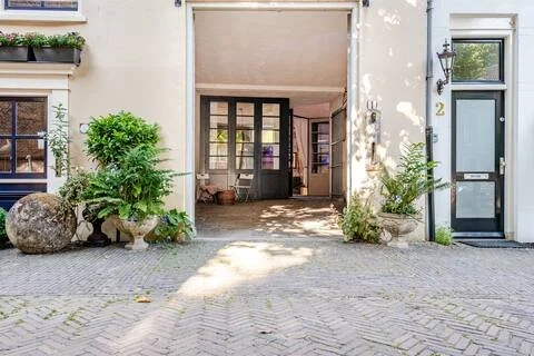 Ingang van een gebouw met planten en een stenen bol voor de deur