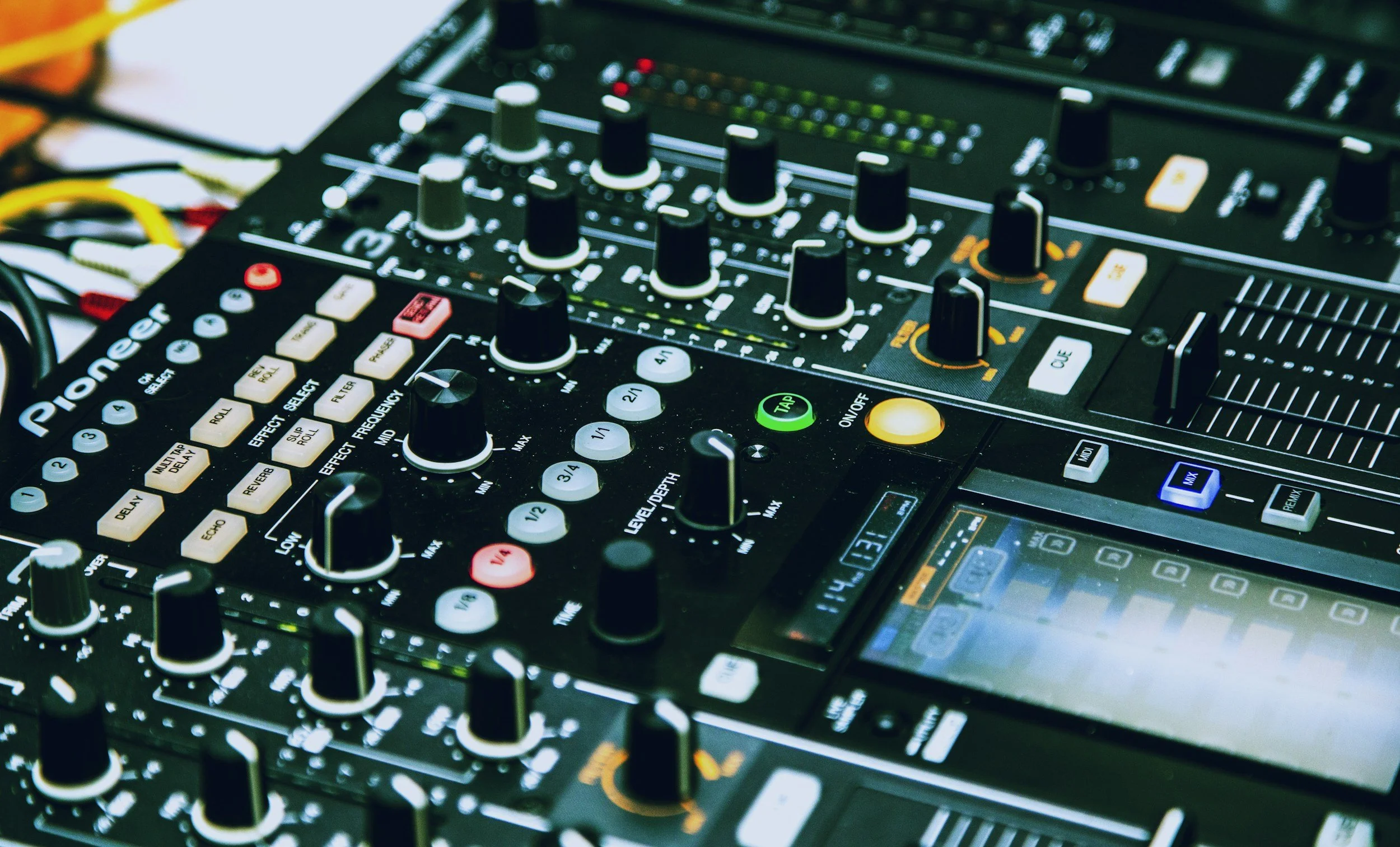 Close-up of a DJ mixing console with various knobs, buttons, sliders and a display screen.