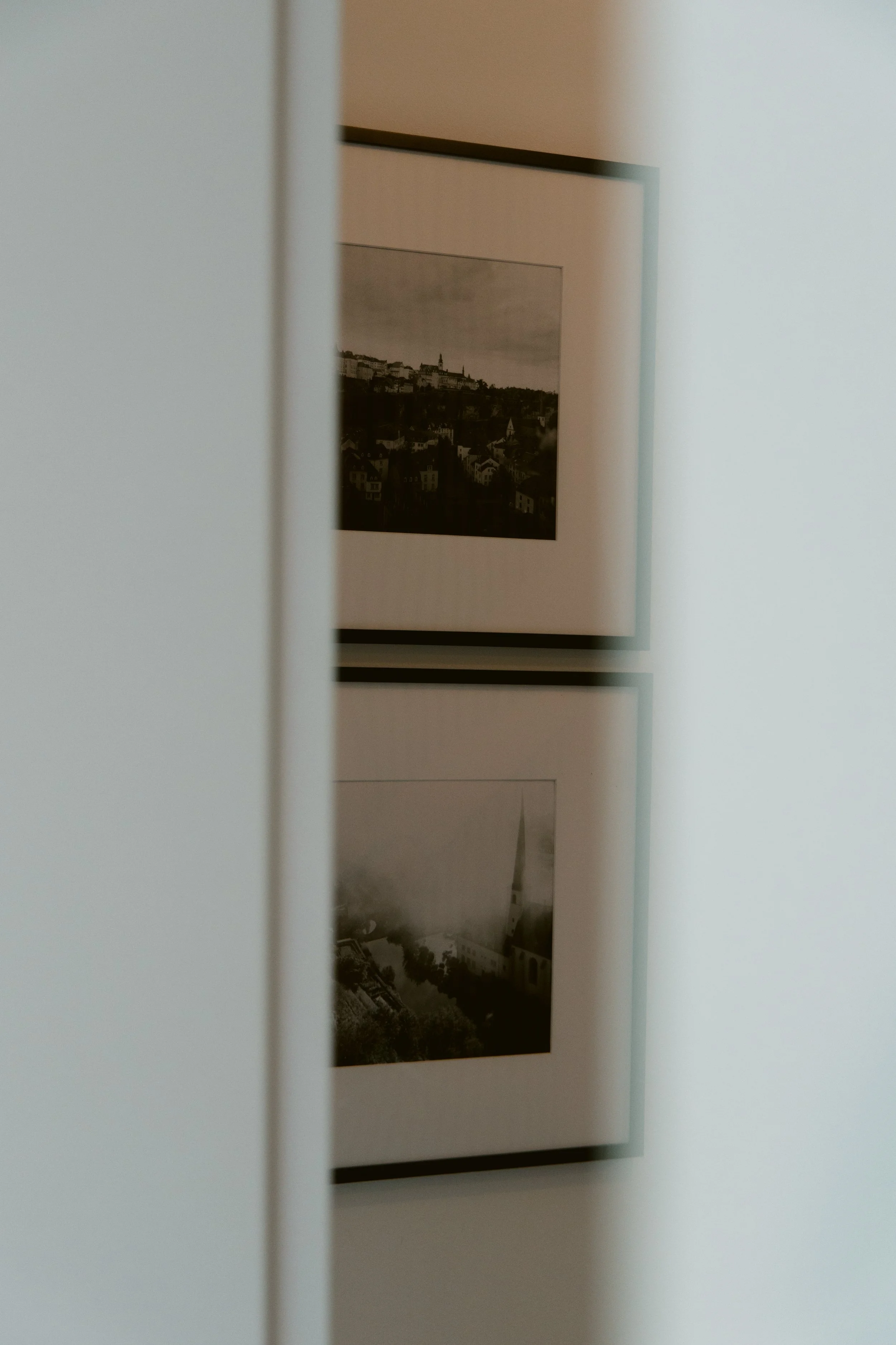 Framed black and white photographs of cityscapes hung on a wall, partially obscured by a white doorframe.