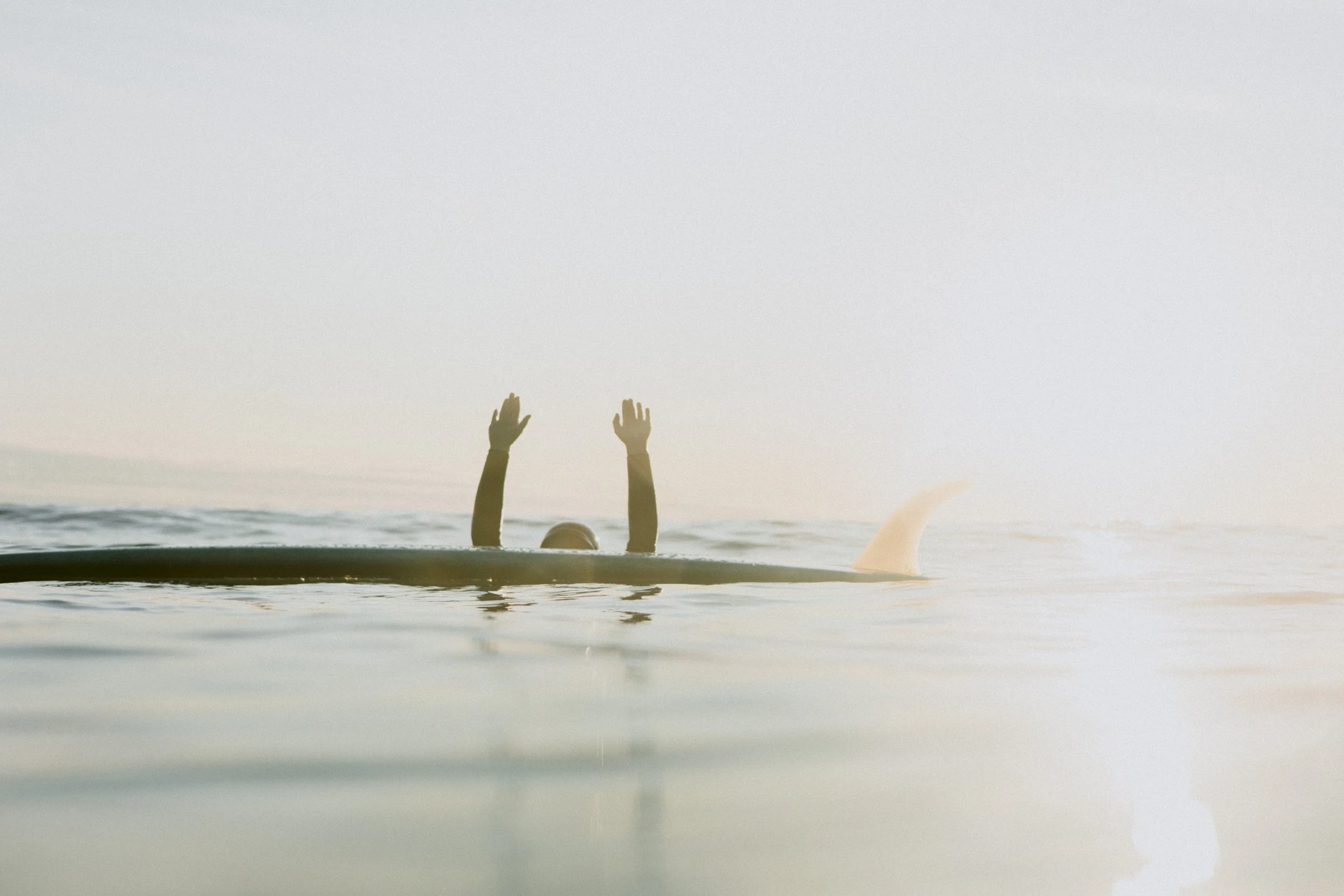 Person swimming in the ocean with just their arms and part of their head visible, raising both hands above the water.
