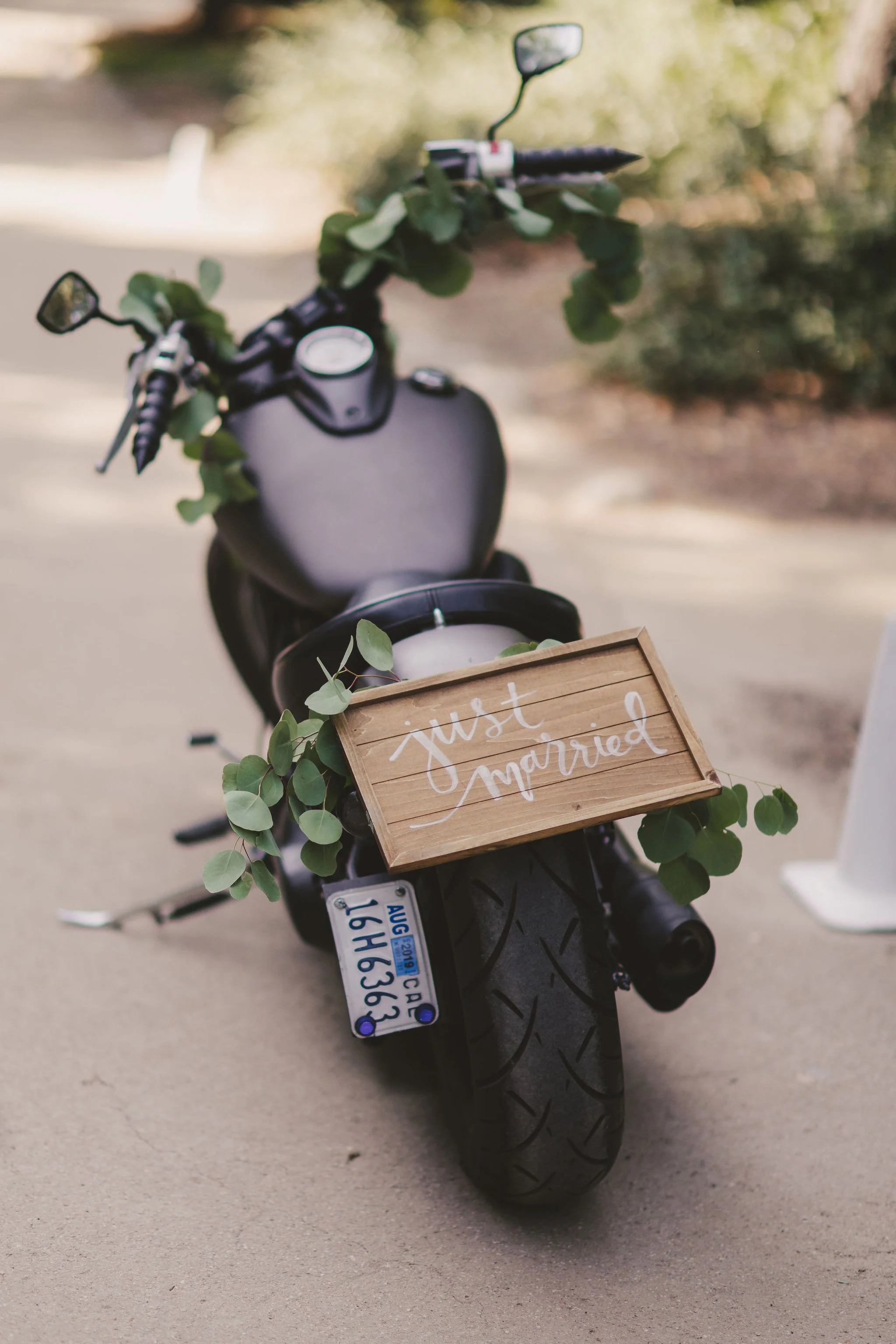 Motorcycle decorated with a wooden "Just Married" sign and greenery.