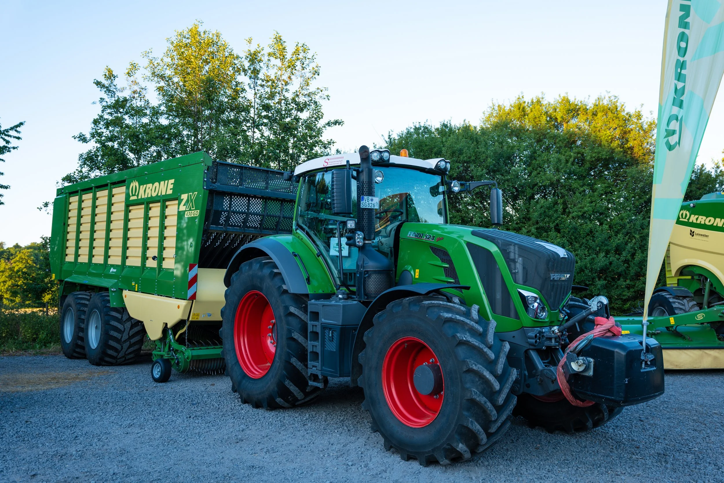 Ein grüner Fendt-Traktor mit einem Krone-Anhänger auf einem Schotterweg.