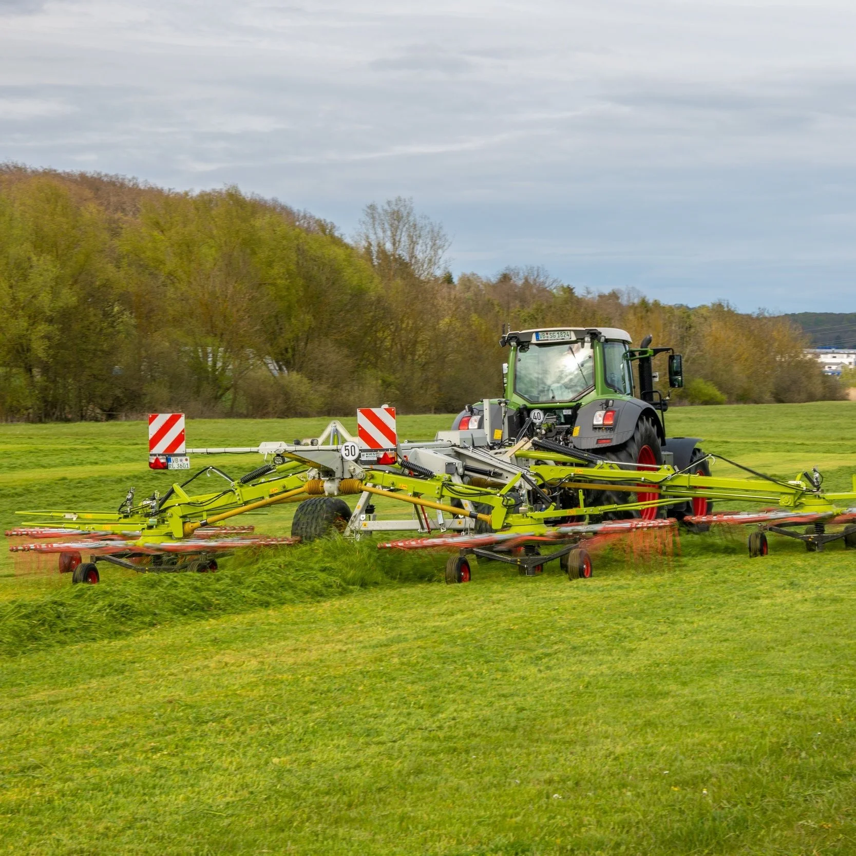 Traktor mit Heuwender auf einem grünen Feld