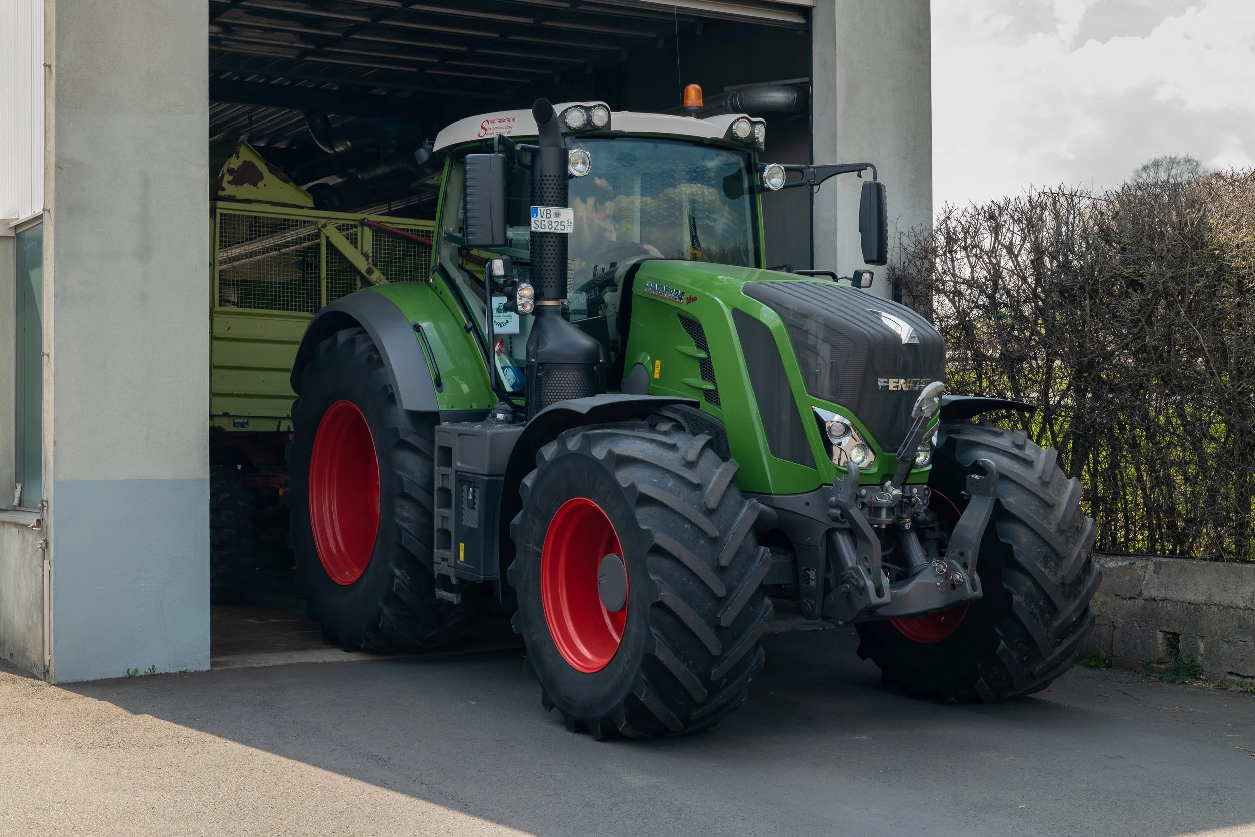 Grüner Traktor, der eine landwirtschaftliche Maschine aus einem Schuppen zieht.