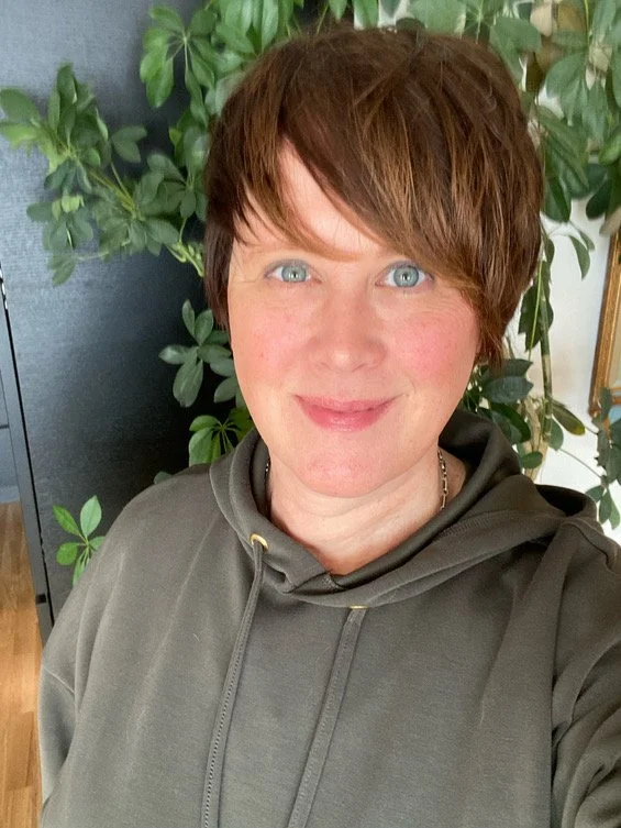 En kvinne i grønn genser som har en grønn plante bak seg. Hun smiler. Hun har forstått noe med det bevisste og ubevisste sinn som flere trenger å høre.