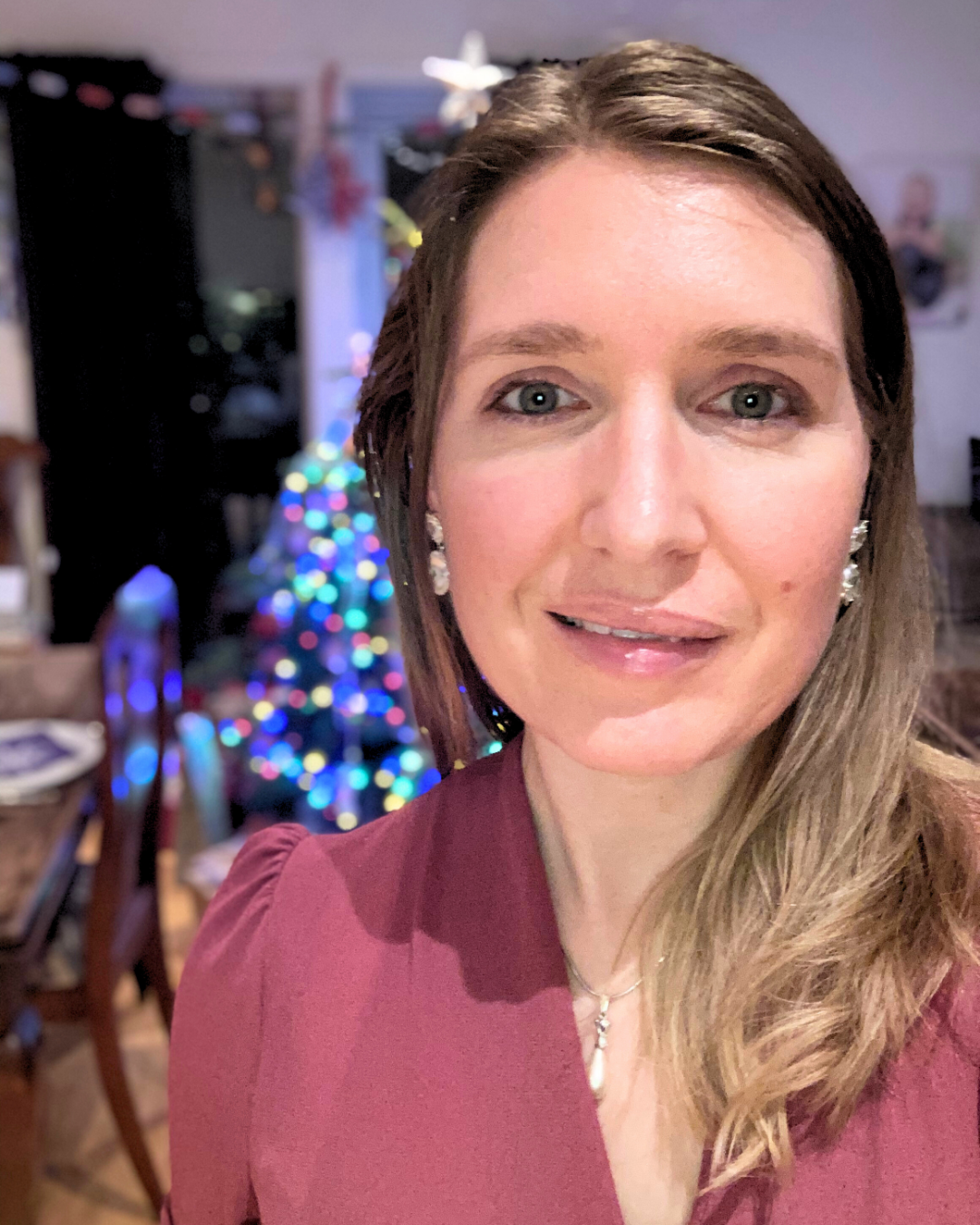 En kvinne som prøver å smile med juletre i bakgrunnen. Jul en en vanskelig tid når du er sensitiv og har autisme.