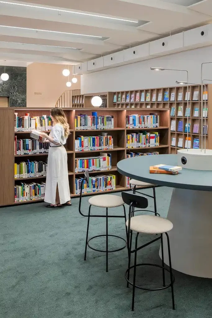Frau mit langen blonden Haaren und weißem Kleid steht an Bücherregal, Biblothek