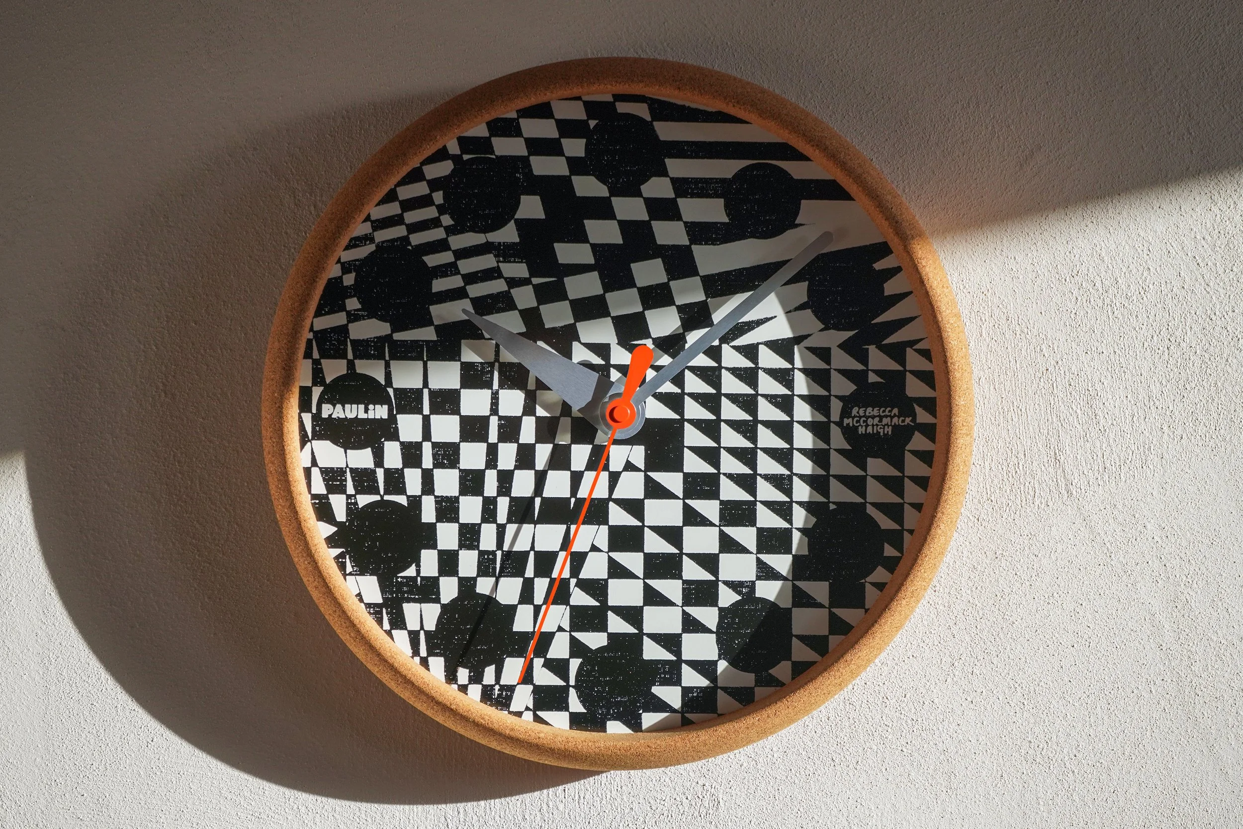 Paulin Dazzle Clock limited edition wall clock featuring a bold geometric black and white screenprinted dial by Rebecca McCormack, housed in a cork case with an orange seconds hand.