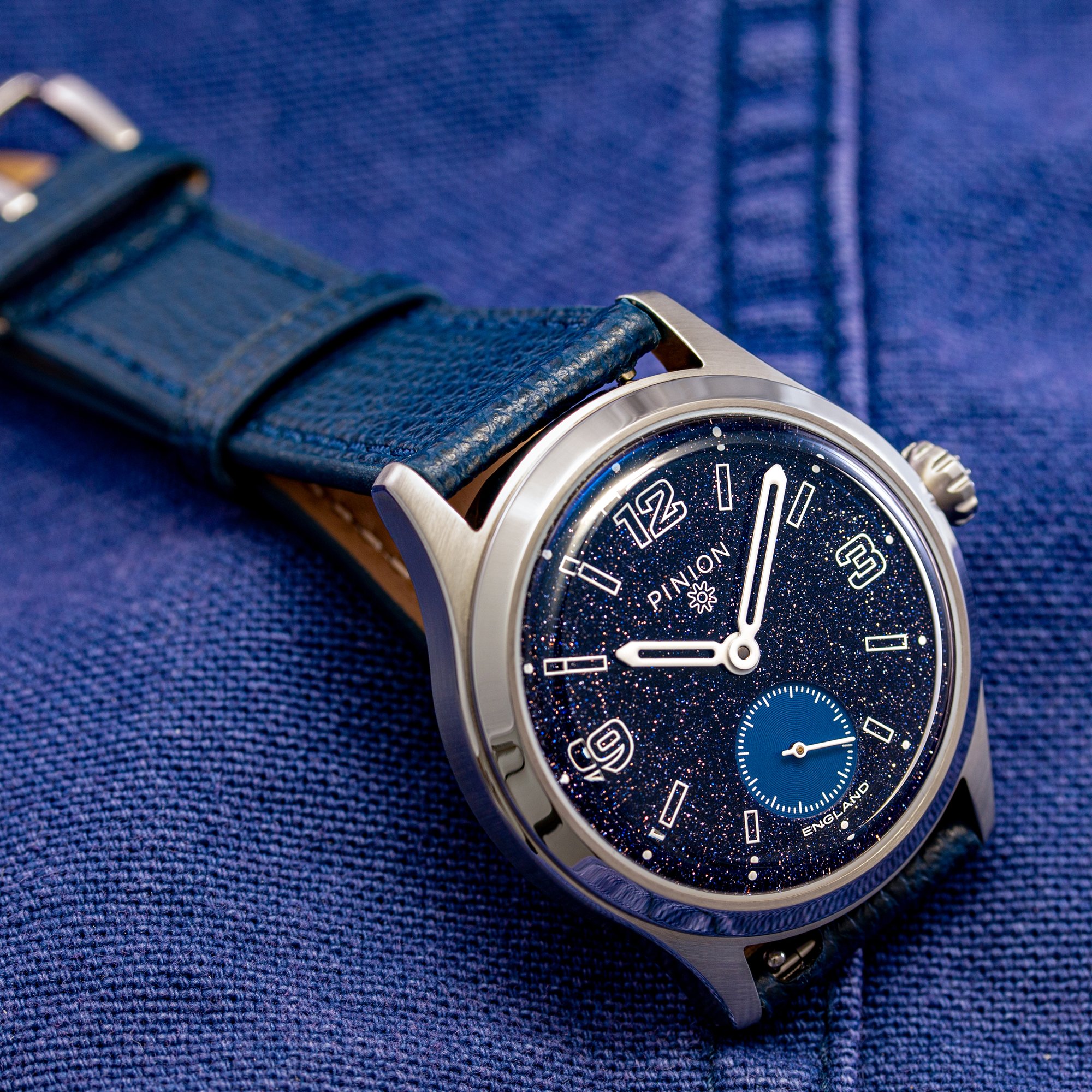 Pinion Pure Chance limited edition watch featuring a sparkling aventurine glass dial with luminous numerals, small seconds sub dial, stainless steel case, and blue leather strap.