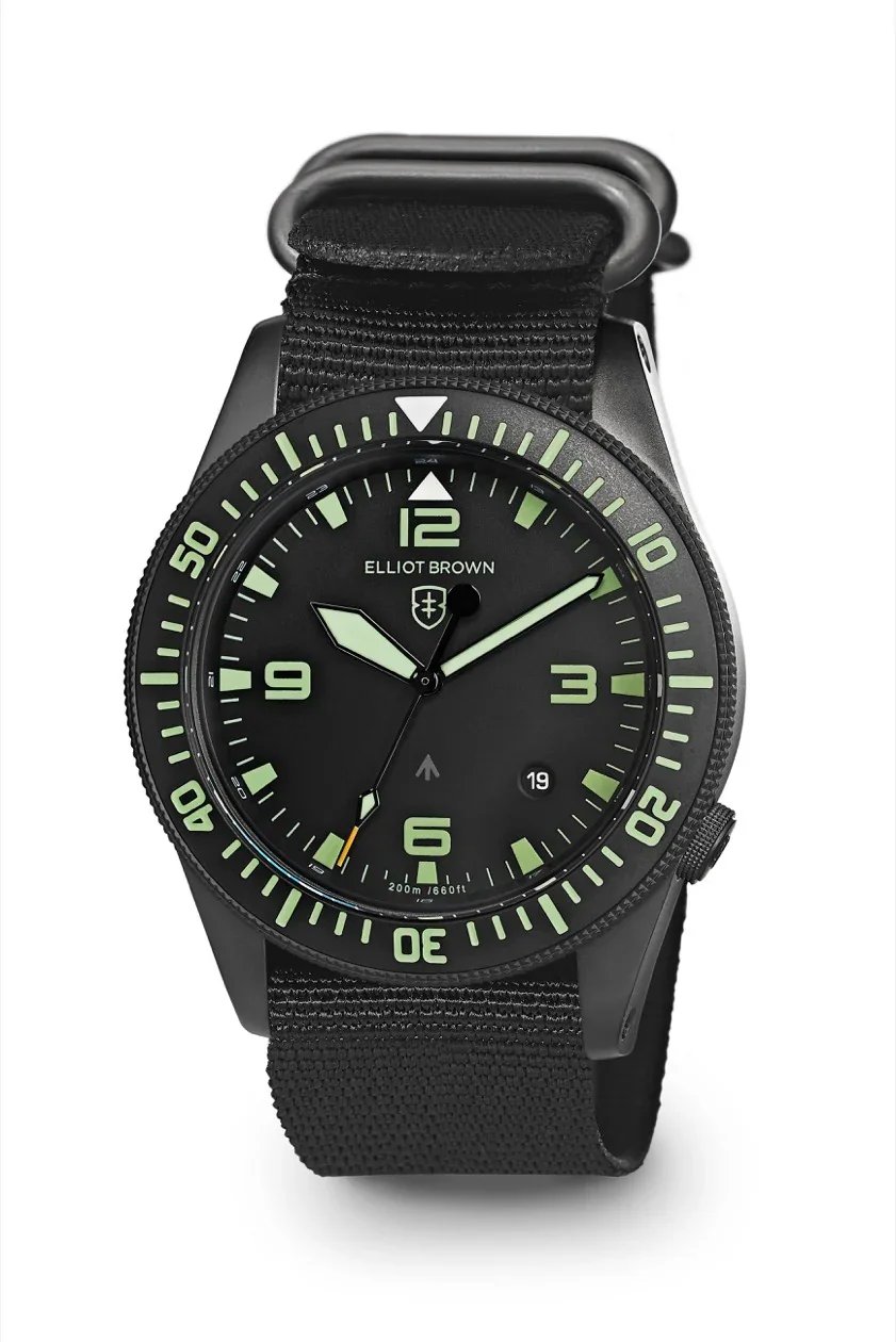 Close-up of the Elliot Brown Holton Professional dive watch featuring a matte black case, black dial with bold green lume markers and numerals, rotating bezel, date window at 4 o’clock, and a black fabric strap.