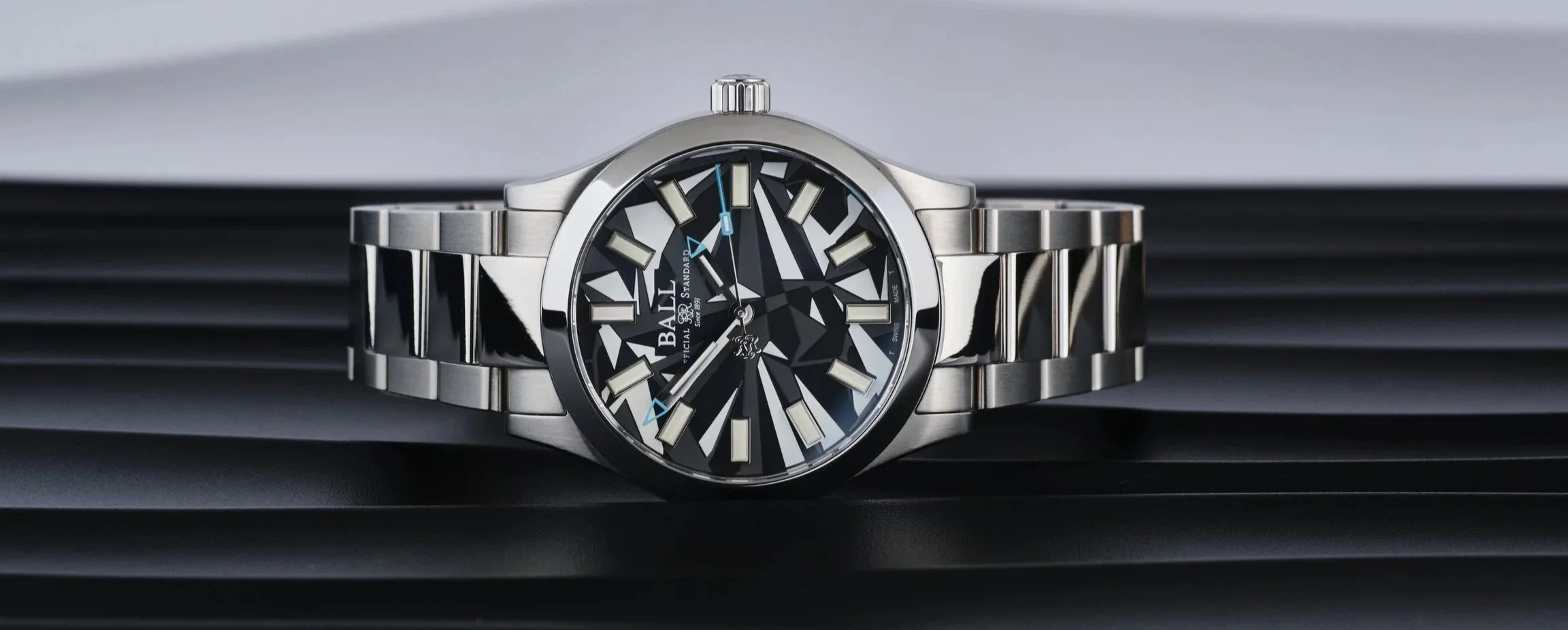 Ball Engineer Dazzle II wristwatch with a black and grey geometric camouflage dial, stainless steel case and bracelet, photographed head-on against a sculpted monochrome background.