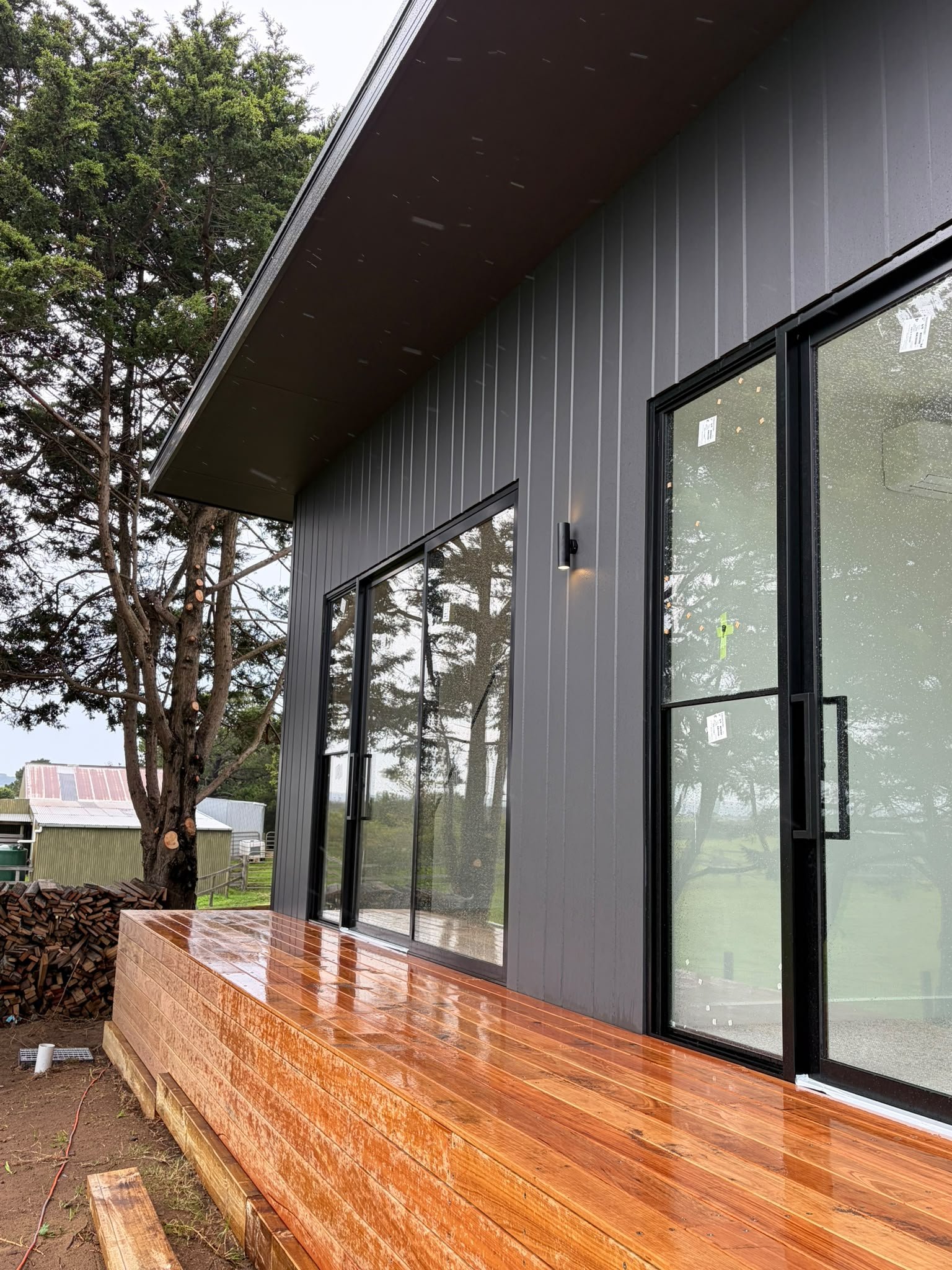 Modern house with black exterior walls, large sliding glass doors, a wooden deck, and trees in the background.