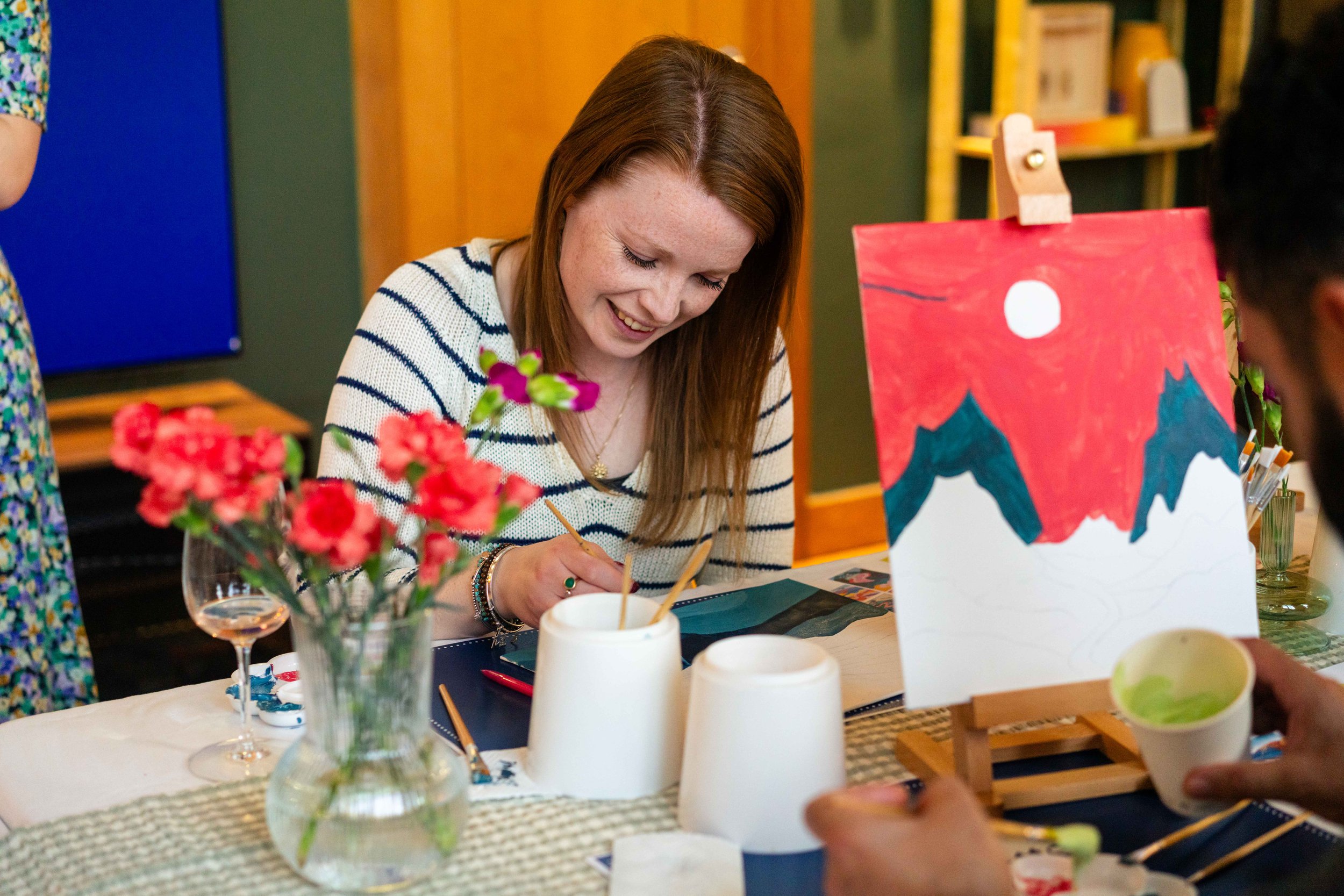 Woman painting at a table with flowers and art supplies.