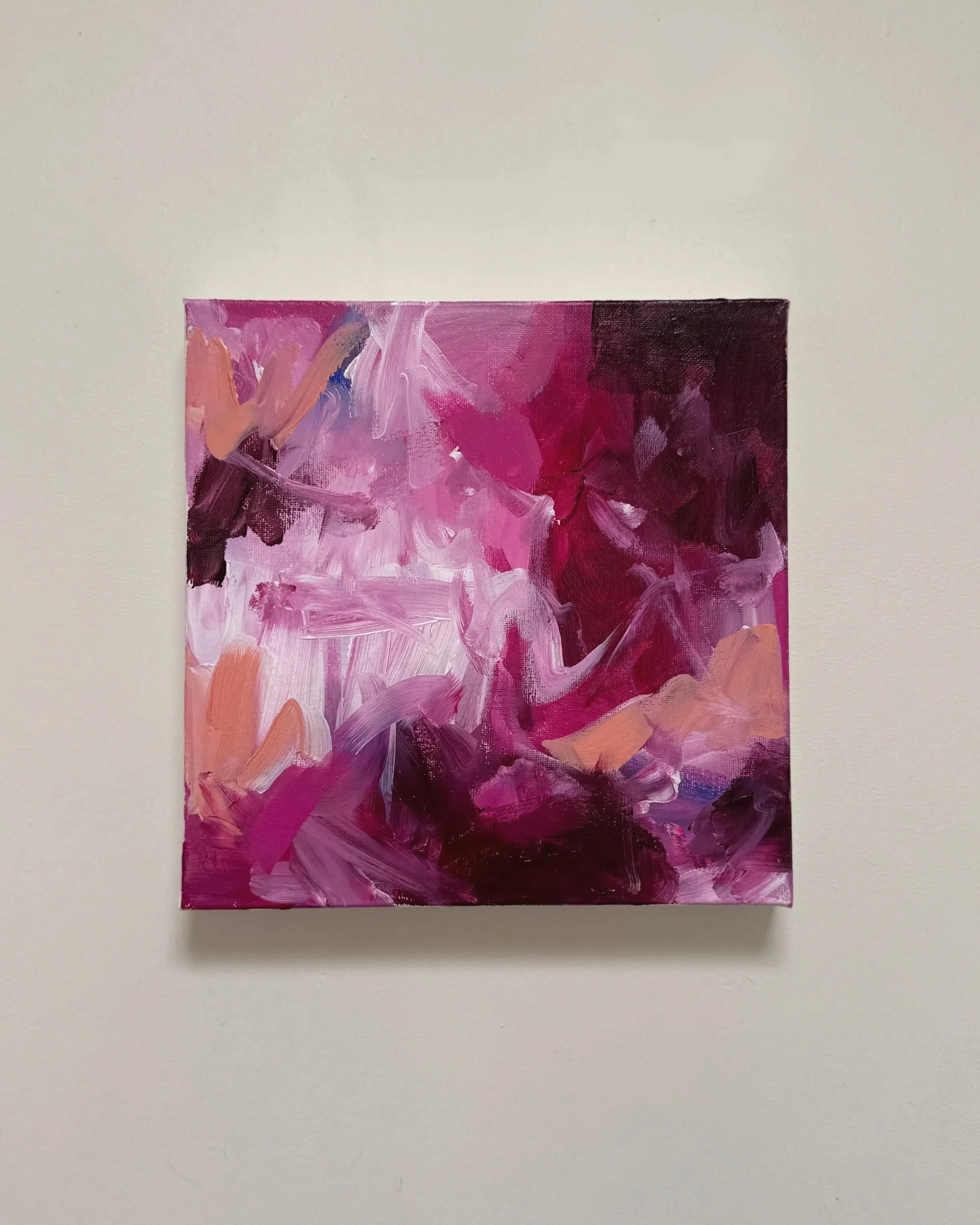 Abstract painting with various shades of pink, purple, and black on a small canvas mounted on a white wall.