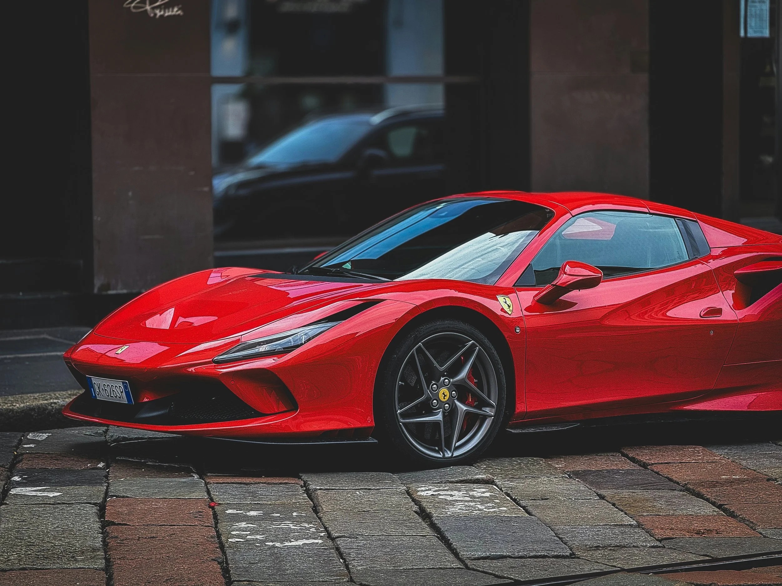 A red Ferrari sports car parked on a brick-paved street.