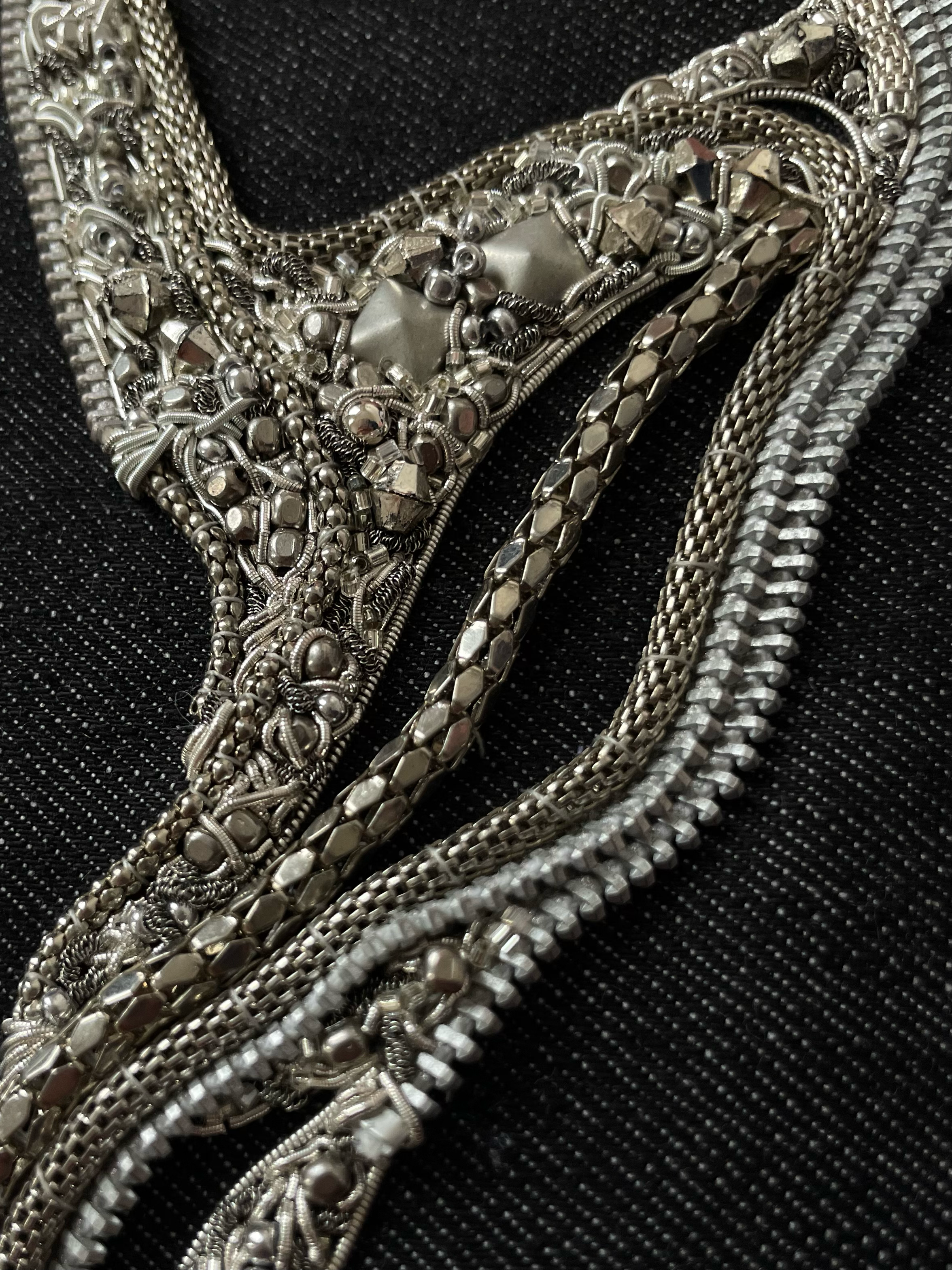 Multiple silver jewelry necklaces with intricate designs, resting on a black textured surface.
