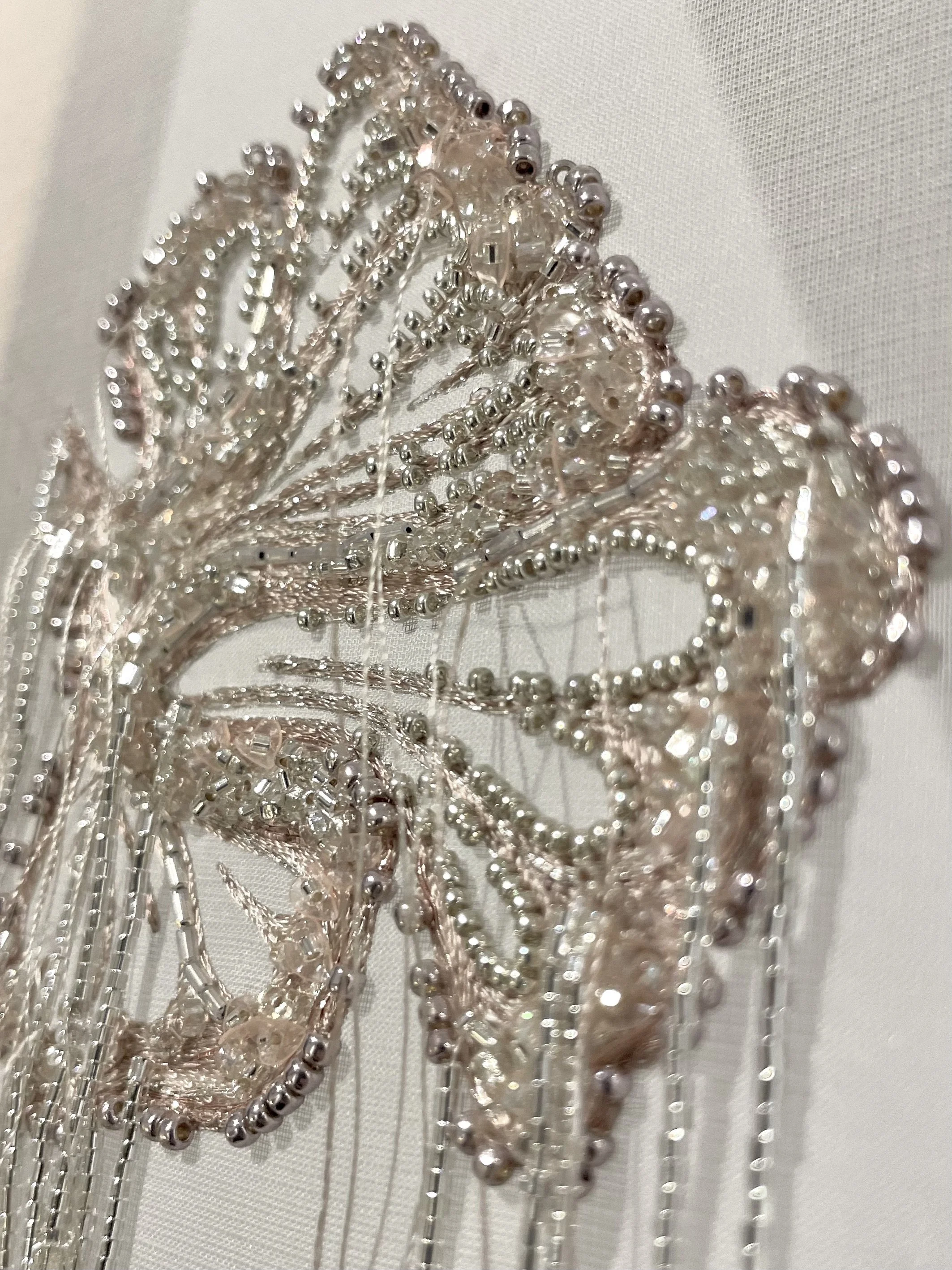 Close-up of a decorative piece with pink and silver beads, arranged in an intricate design on a white textured surface.