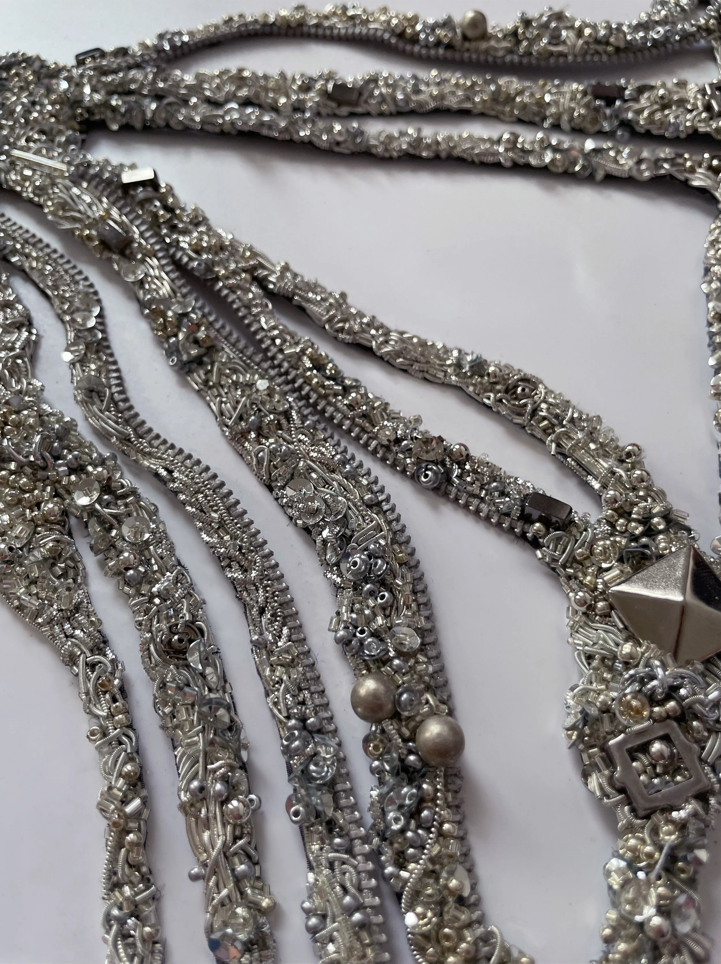 Multiple silver necklaces with various intricate designs and bead patterns, some with large decorative elements, laid out on a white surface.