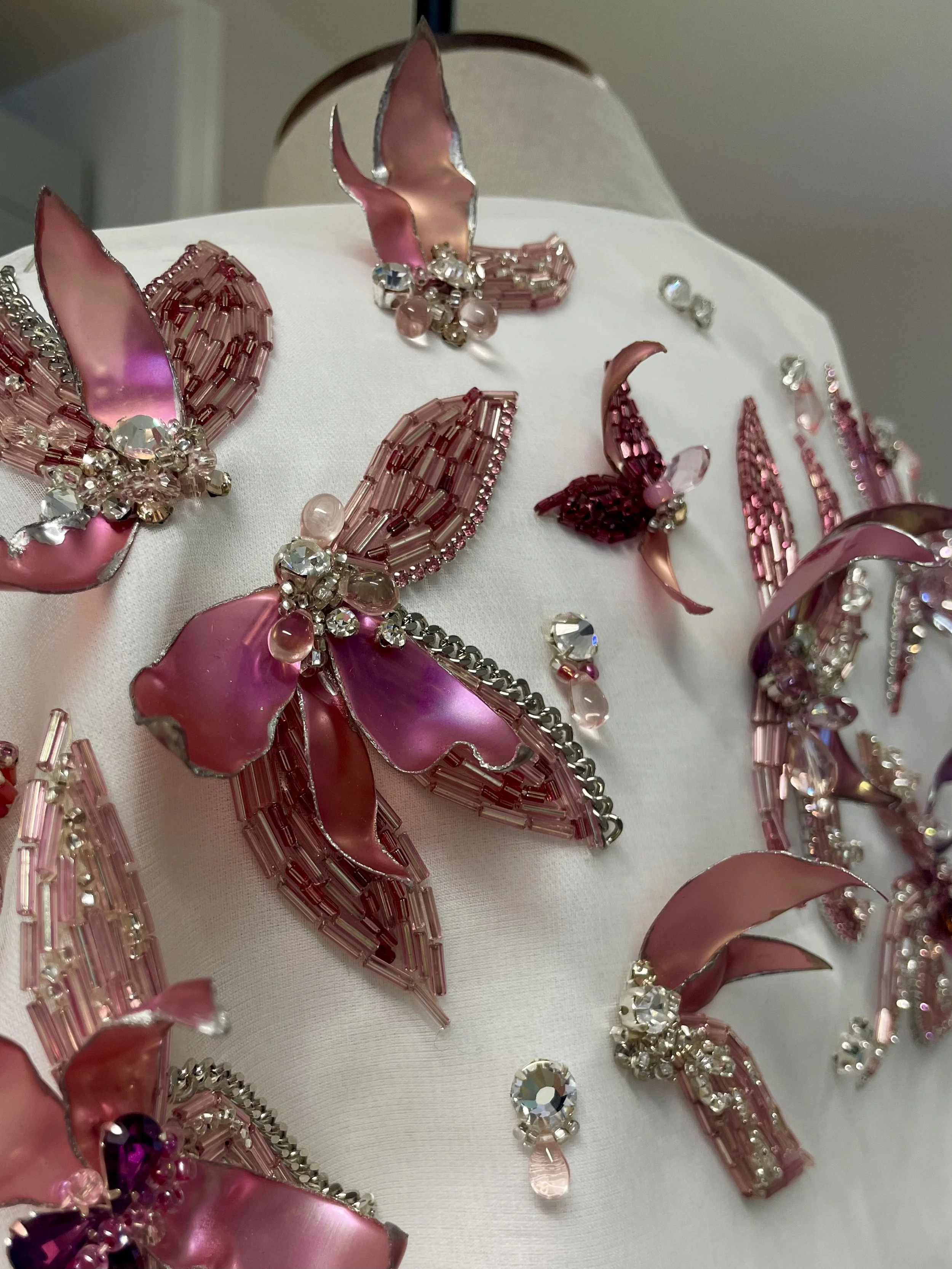 Close-up of pink and clear rhinestone butterfly-shaped jewelry on a white fabric surface.